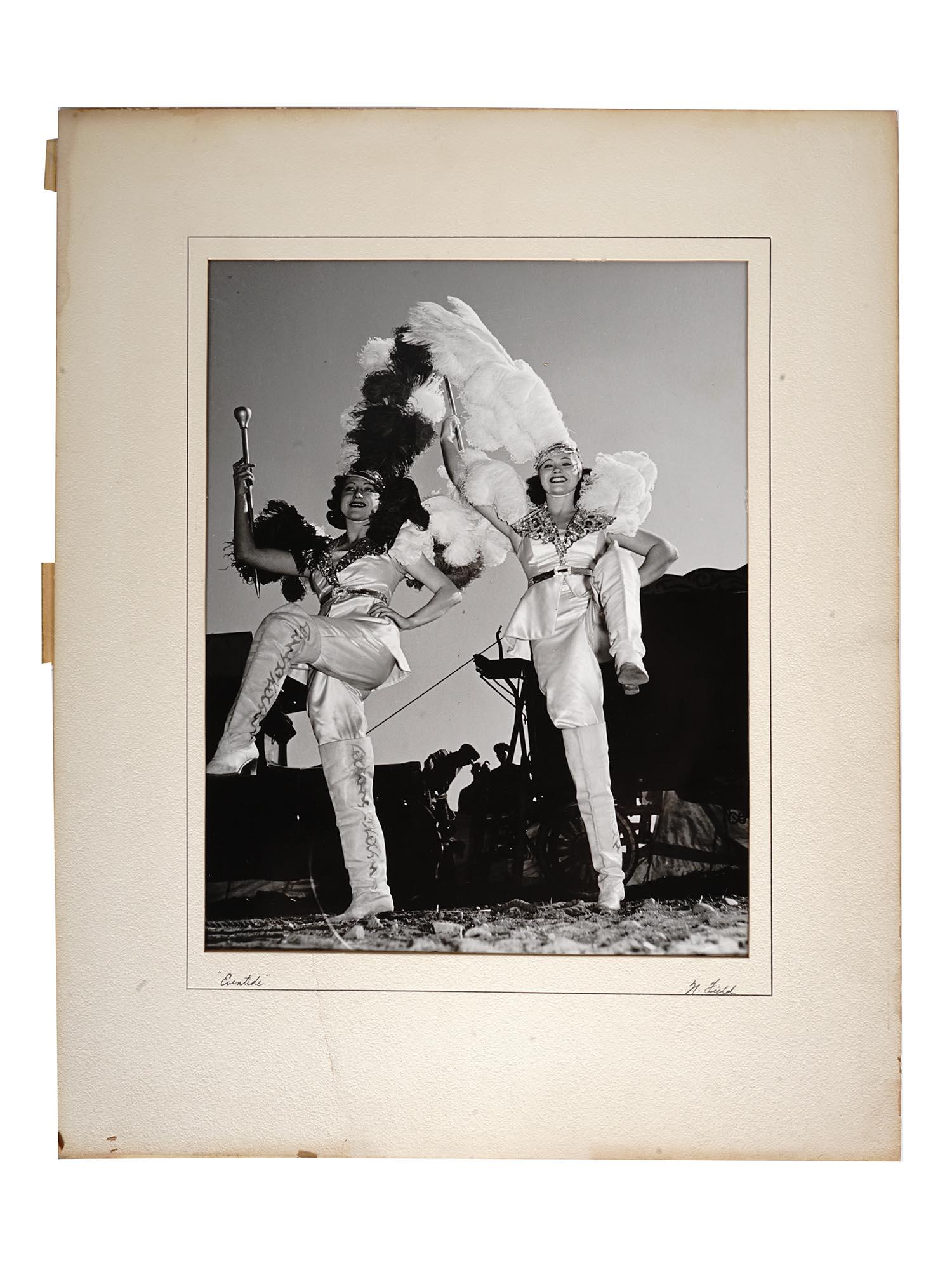 1940S PHOTO OF CIRCUS DANCERS BY NATHANIEL FIELD: A mid-century black and white photo print of two female circus dancers. White mat. Titled Eventide in the lower left. Hand-signed N. Field in the lower right. Inscription on the backside: This print w
