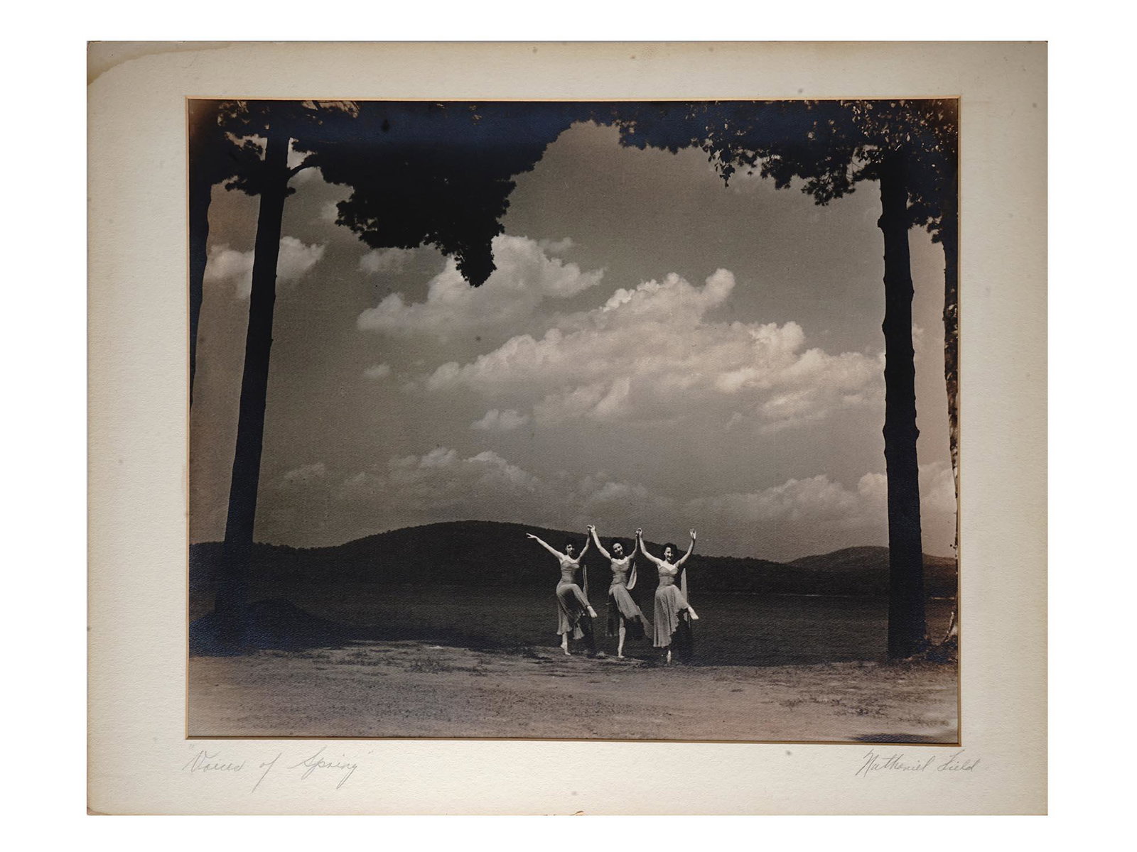 1940S PHOTOGRAPH THREE DANCERS BY NATHANIEL FIELD: A mid-century black and white photo print of three female dancers against a landscape. White mat. Titled Voices of Sping No.2 in the lower left. Hand-signed Nathaniel Field in the lower right. Nathani