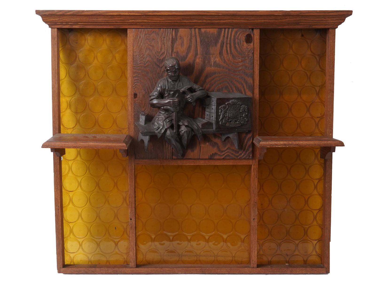 YELLOW BOTTLE GLASS WALL SHELF WITH METAL RELIEF: A vintage handmade wall shelf. A carved wooden framework with two small shelves and a central panel on which a metal relief is fixed. The relief depicts a carpenters and a coat of arms with the letter