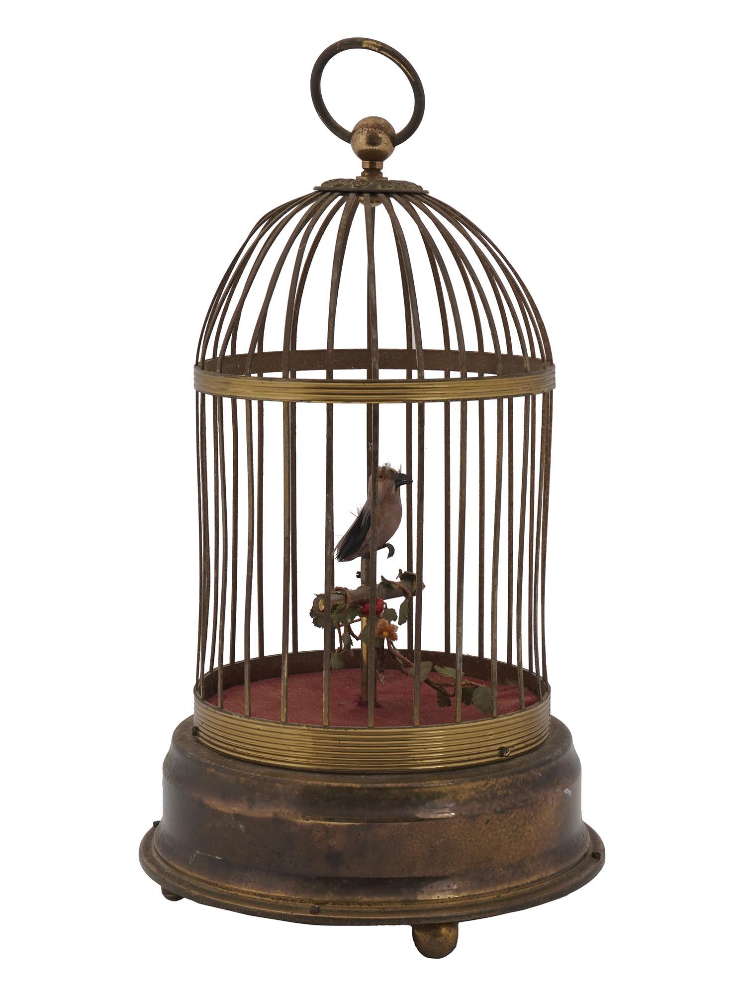 VINTAGE GERMAN MUSICAL SINGING BIRD BRASS CAGES: A vintage German musical automaton singing birds in a brass cage. The gold finish cage features a bird with real pink and yellow feathers. A hanging loop on the top. Unmarked. Circa: Mid 20th century.