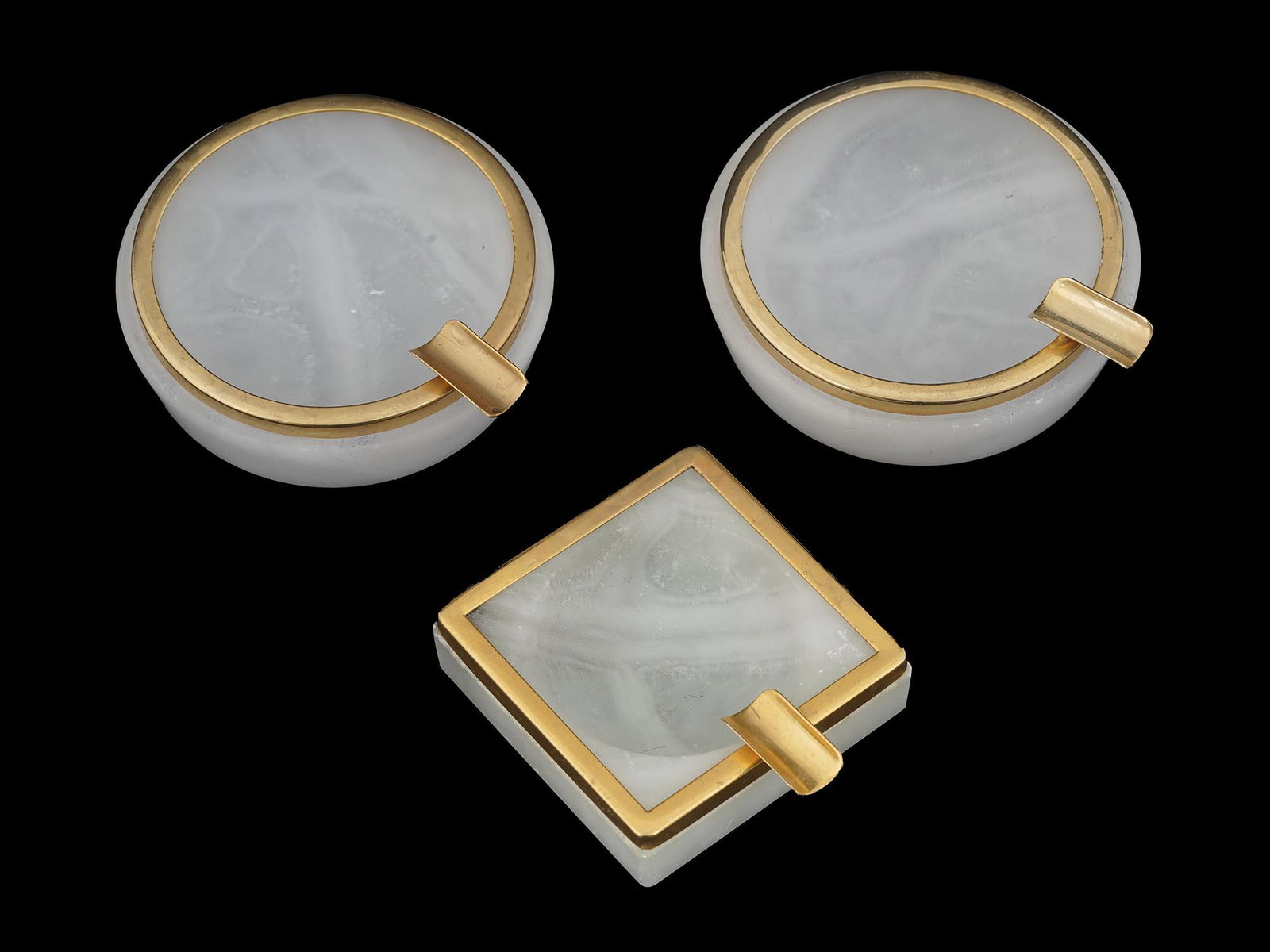 CAMBODIAN CARVED WHITE MARBLE AND GOLD ASHTRAYS: A lot of three matching ashtrays from Phnom Penh, Cambodia. The pieces are made of carved white marble and have golden rims and cigarette holders. Round and square shapes. Each item has an etched mode