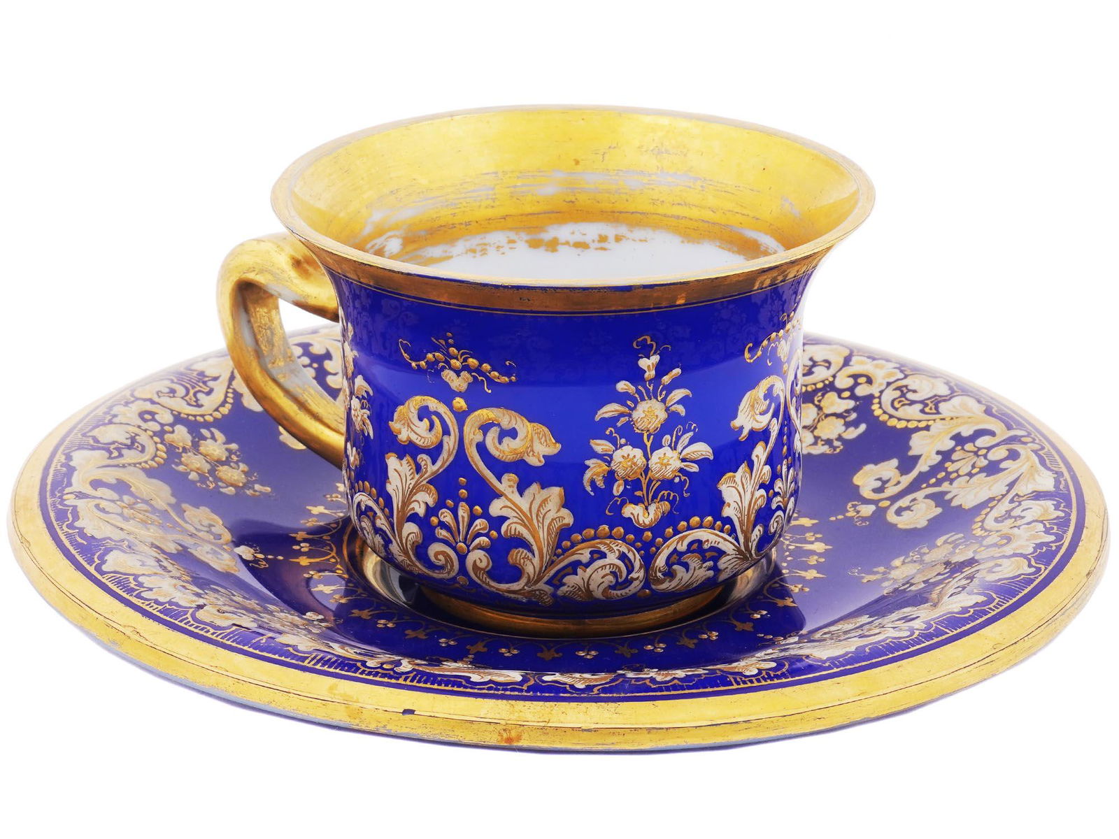 ANTIQUE RUSSIAN GILT OPALINE GLASS CUP AND SAUCER: An Imperial Russian cobalt blue opaline glass tea pair. The items are richly decorated with a hand-painted golden floral ornament. The rims are gilt. Collectible Glassware Tableware Serveware Tea Serv