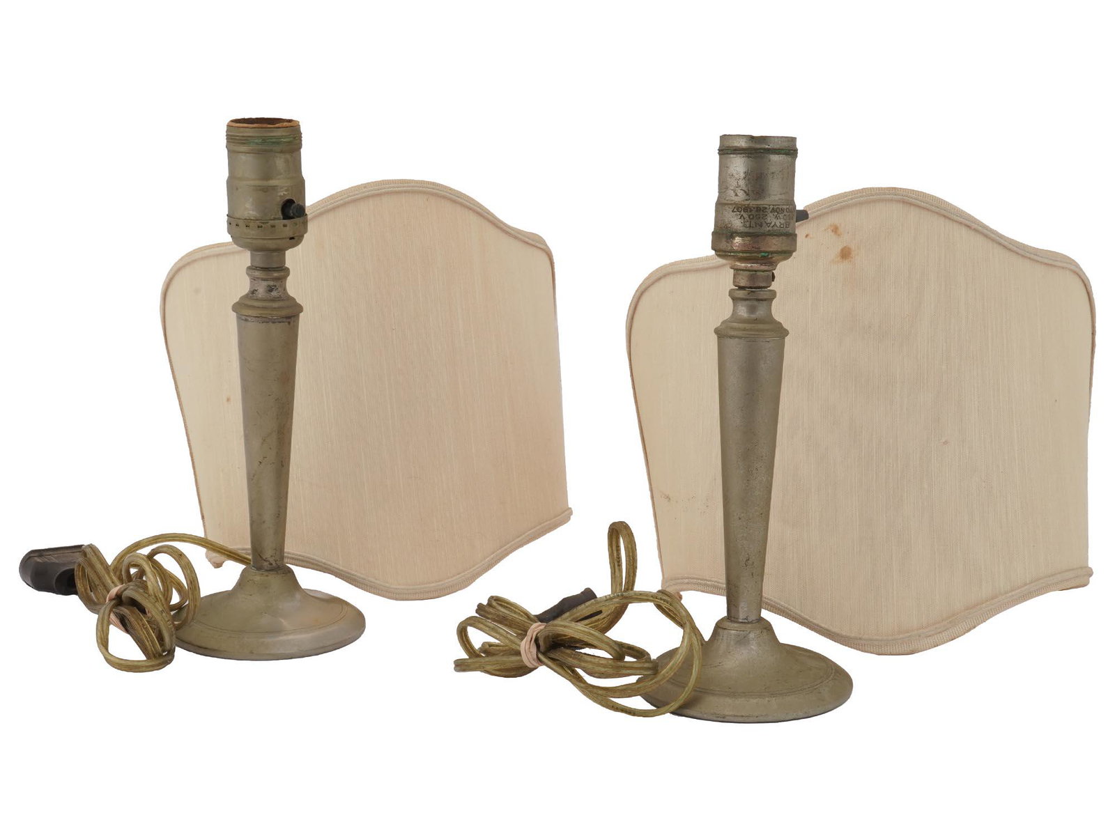 PAIR OF ANTIQUE BRYANT TABLE LAMPS WITH SHADES: A pair of identical antique early 20th-century American electrical table lamps. The brass lamps have a single light socket and half-round beige lamp shades. Hallmark Bryant 250 V Pat. Nov. 26 1907 is