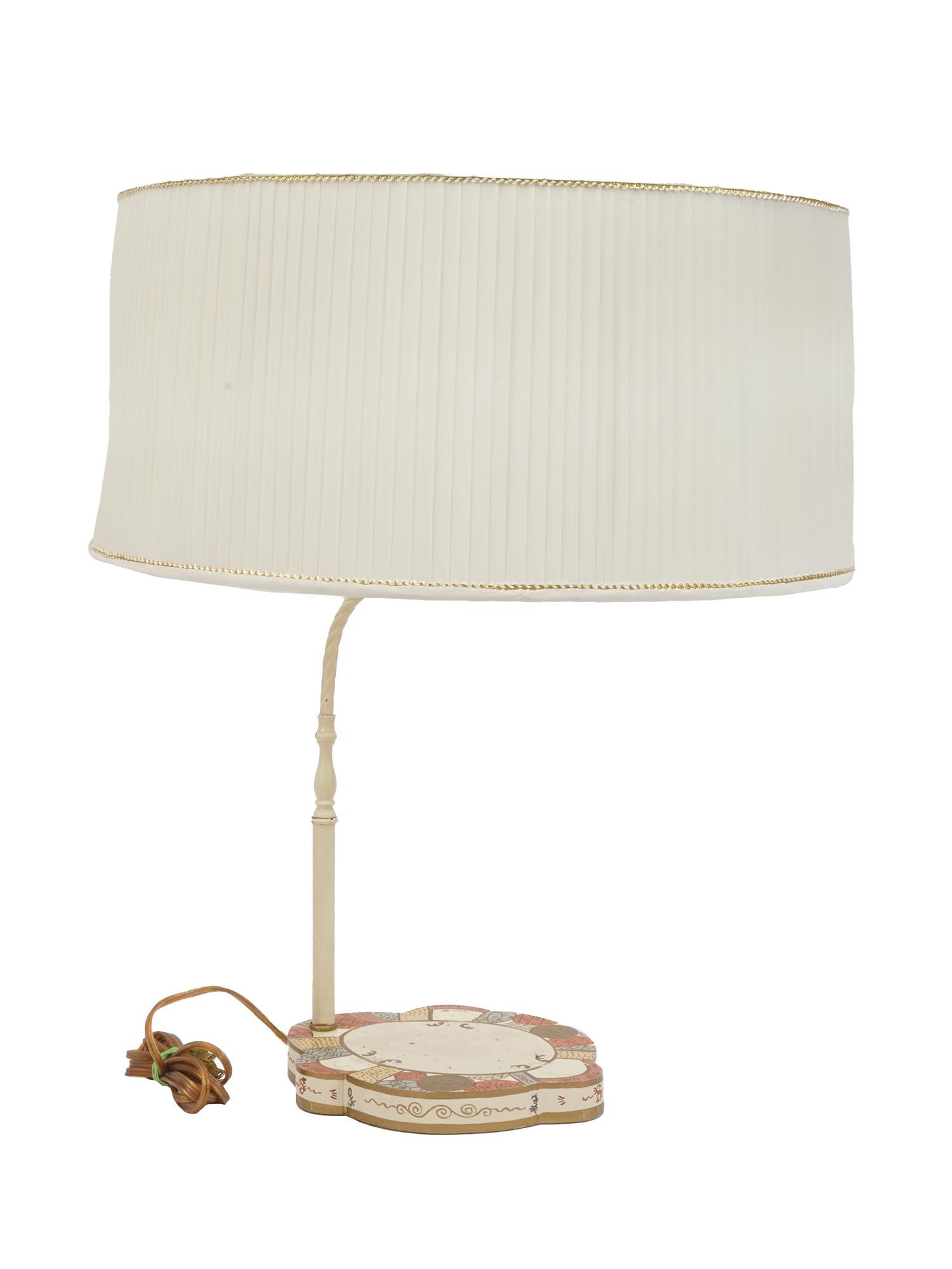 HAND PAINTED TABLE LAMP WITH BEIGE PLEATED SHADE: A vintage table lamp. The piece has a hand-painted wooden base with pastel and golden ornaments. White wooden shaft holds a single light socket. The item has a simple beige pleated fabric lampshade. V