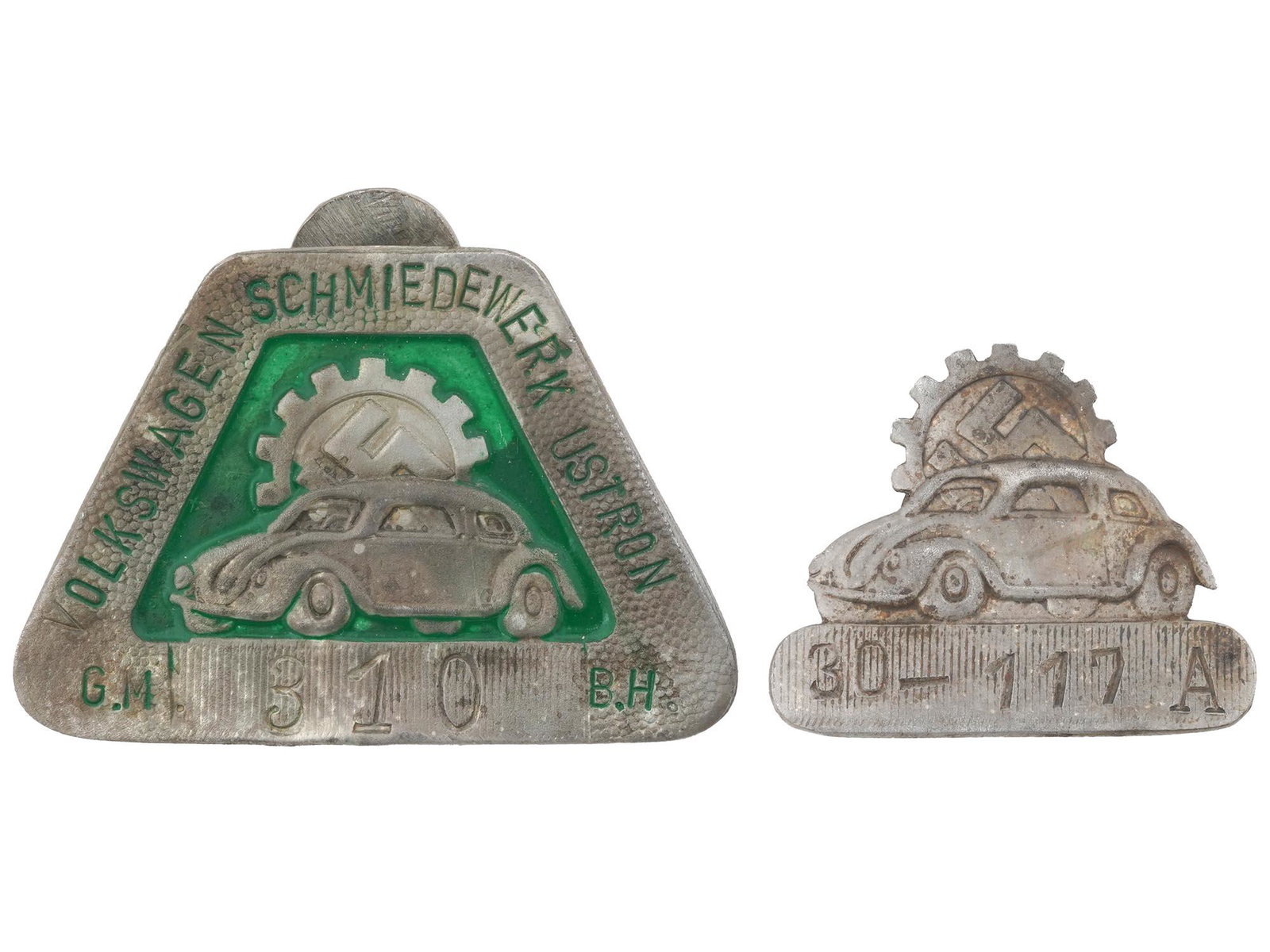 WWII GERMAN VOLKSWAGEN FACTORY EMPLOYEE SHIELDS: A WWII Nazi German Volkswagen factory employee shields. The first: is a green enameled shield featuring an image of a car with a swastika insignia behind, numbered with etching, 310, below, and an ins