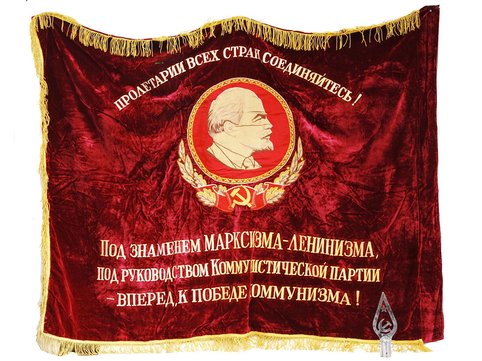 SOVIET EMBROIDERED BANNER AND STEEL FLAG POMMEL: A Soviet red velvet banner with golden fringe. The item is decorated with an embroidered portrait of Vladimir Lenin, the sickle and hammer emblem, and inscription in Russian: Proletarians of All Count