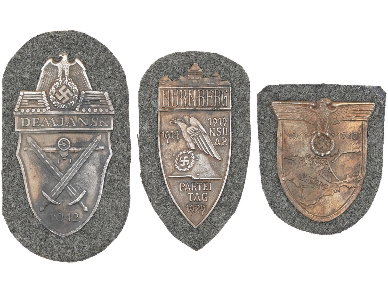 GROUP OF WWII NAZI GERMAN MILITARY SHIELDS 3 PCS: A group of three World War II German military decorations. First, a World War II German military decoration, the Demyansk Shield, Armelschild Demjansk in German. The zinc badge features an eagle with 