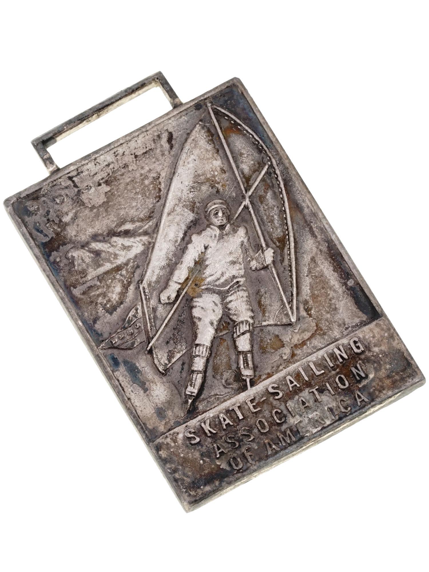 1929 AMERICAN SKATE SPORTS MEDAL, STERLING SILVER: An antique American early 20th century silver oblong badge with rectangular section suspension loop. The obverse showing a skater with sails, the plain tablet below features an engraved inscription: S