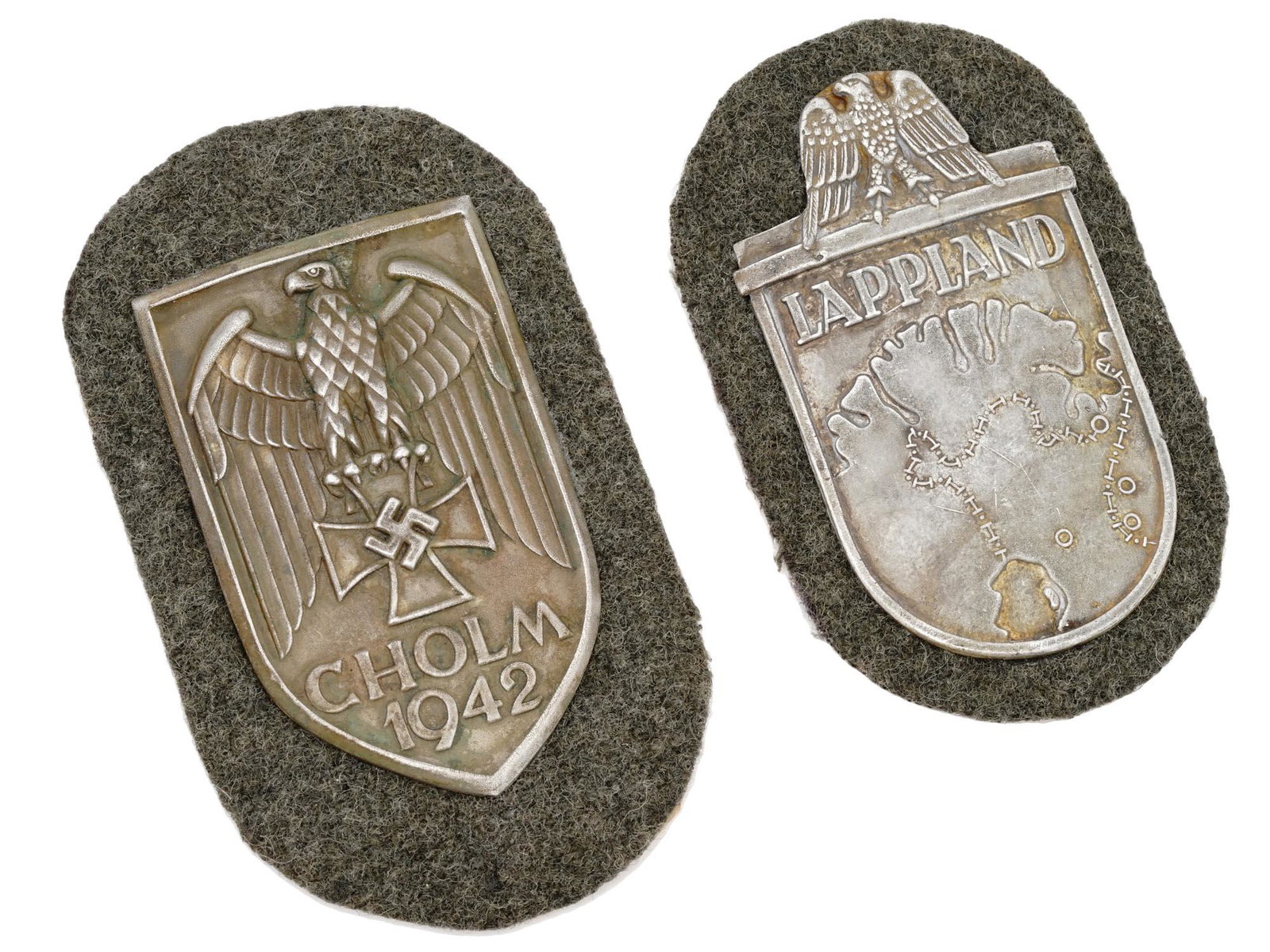 WWII GERMAN MILITARY CHOLM AND LAPLAND SHIELDS: A pair of WWII German military decorations, the Cholm Shield and the Lapland Shield. The Cholm Shield, the rarest of the German combat shields, features a shield, with a large open-winged Wehrmacht st