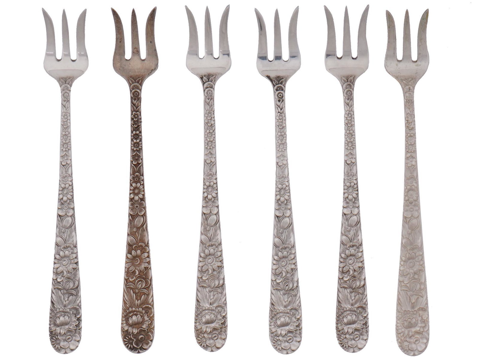 ANTIQUE AMERICAN SILVER COCKTAIL FORKS BY S. KIRK: A set of six antique American Samuel Kirk & Son silver cocktail forks. All pieces feature repousse handles decorated with floral motifs and hallmarked sterling silver. Circa the 1920s. Total weight: 1