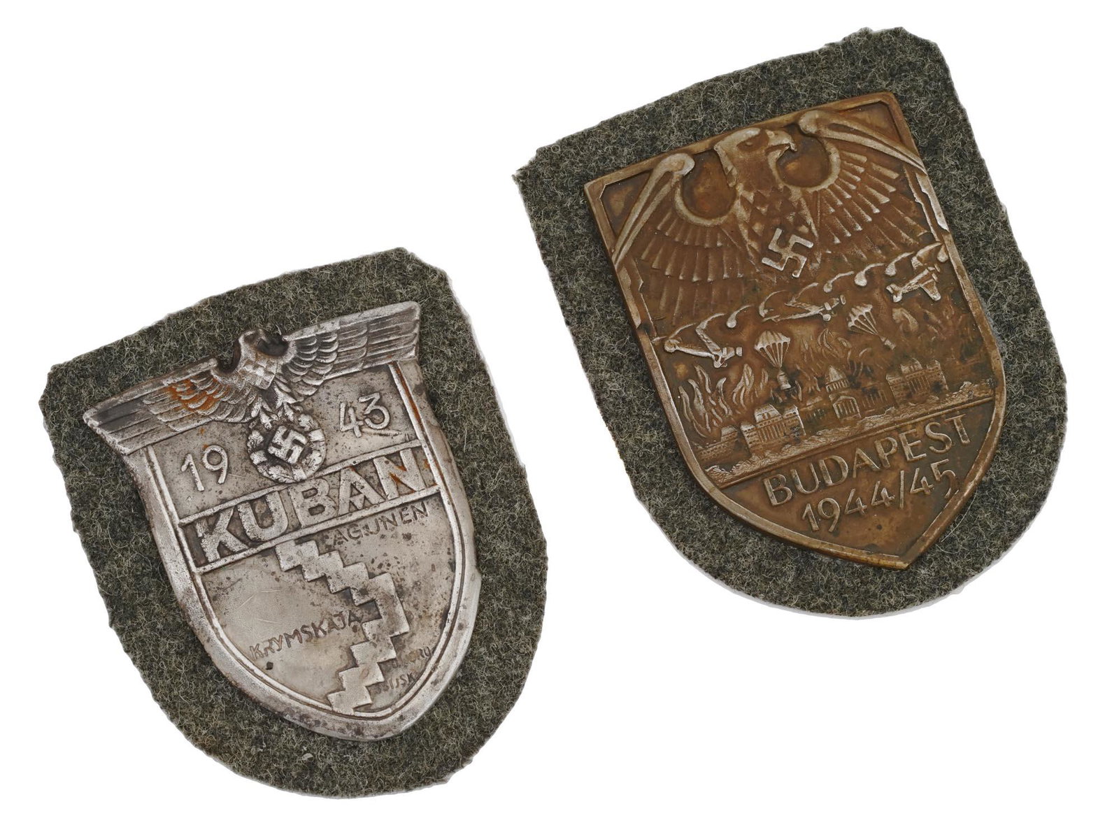 GERMAN WWII KUBAN AND BUDAPEST MILITARY SHIELDS: A pair of WWII Nazi German Third Reich Military shields. The first: a 1943 Kuban sleeve shield, inscribed in German, Kuban Lagunen Crimean Novorossiysk, and a relief image of a Nazi eagle clutching a 