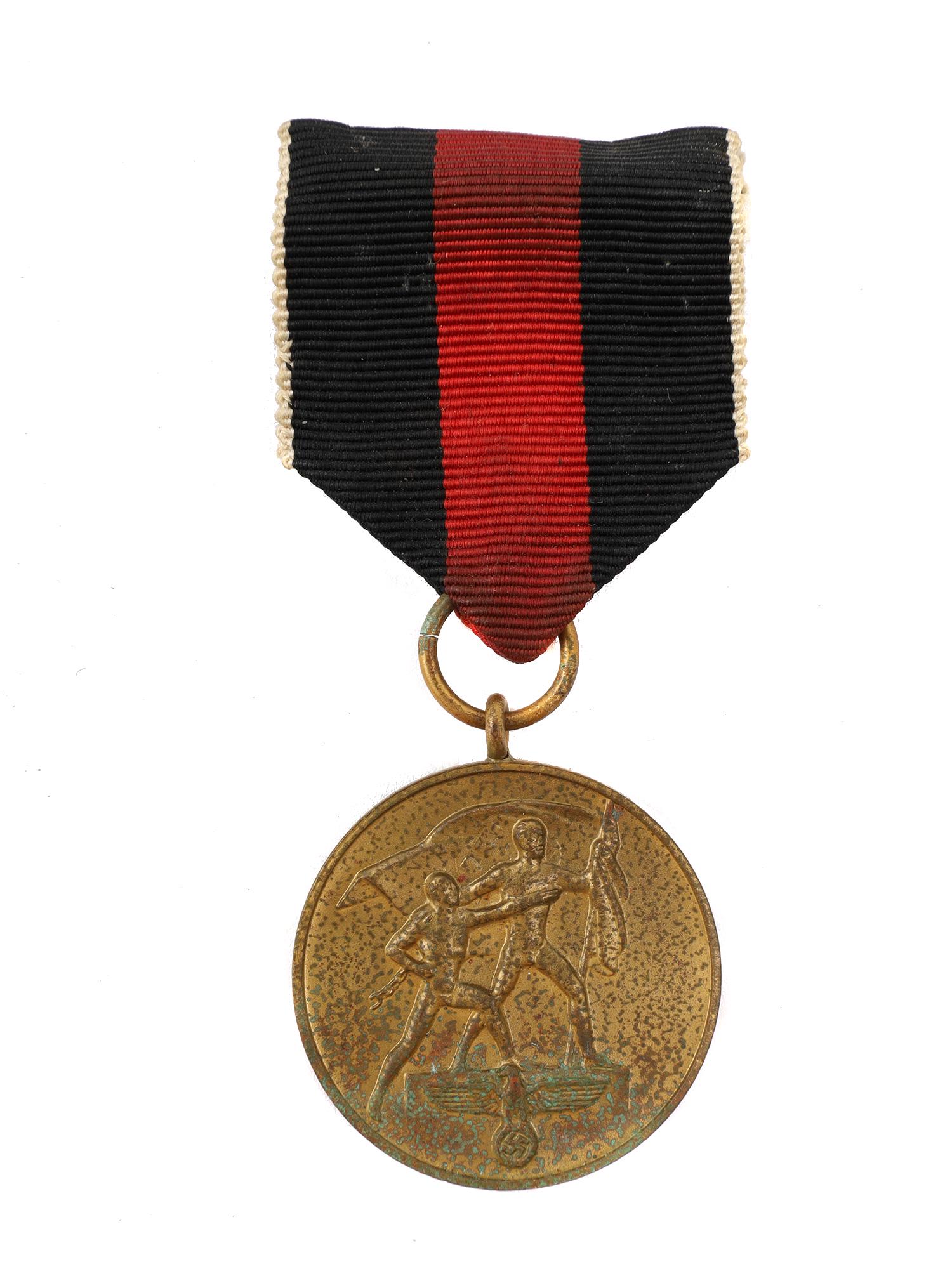 NAZI GERMAN 1938 COMMEMORATIVE SUDETENLAND MEDAL: A Nazi German 1938 Commemorative Medal, known as the Sudetenland Medal. The medal is circular and similar in appearance to the Anschluss Medal. On the obverse: a man holding the Nazi flag stands on a 