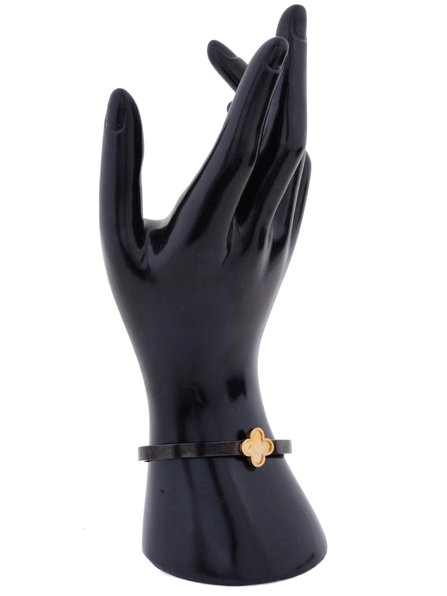 ALHAMBRA STAINLESS STEEL HINGED BANGLE BRACELET: A vintage black stainless steel hinged bangle bracelet. The front of the piece is decorated with a gilt quatrefoil resembling the motif of the Alhambra collections by Van Cleef and Alpers. Marked Stai