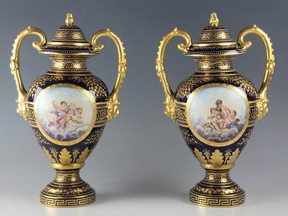 PAIR OF ANTIQUE 19 C ROYAL VIENNA PORCELAIN URNS: An antique 19th century pair of Royal Vienna porcelain vases or lidded urns. Superior hand painted gold decoration surrounding the cartouche with playing putti on each side, features large twin gold c