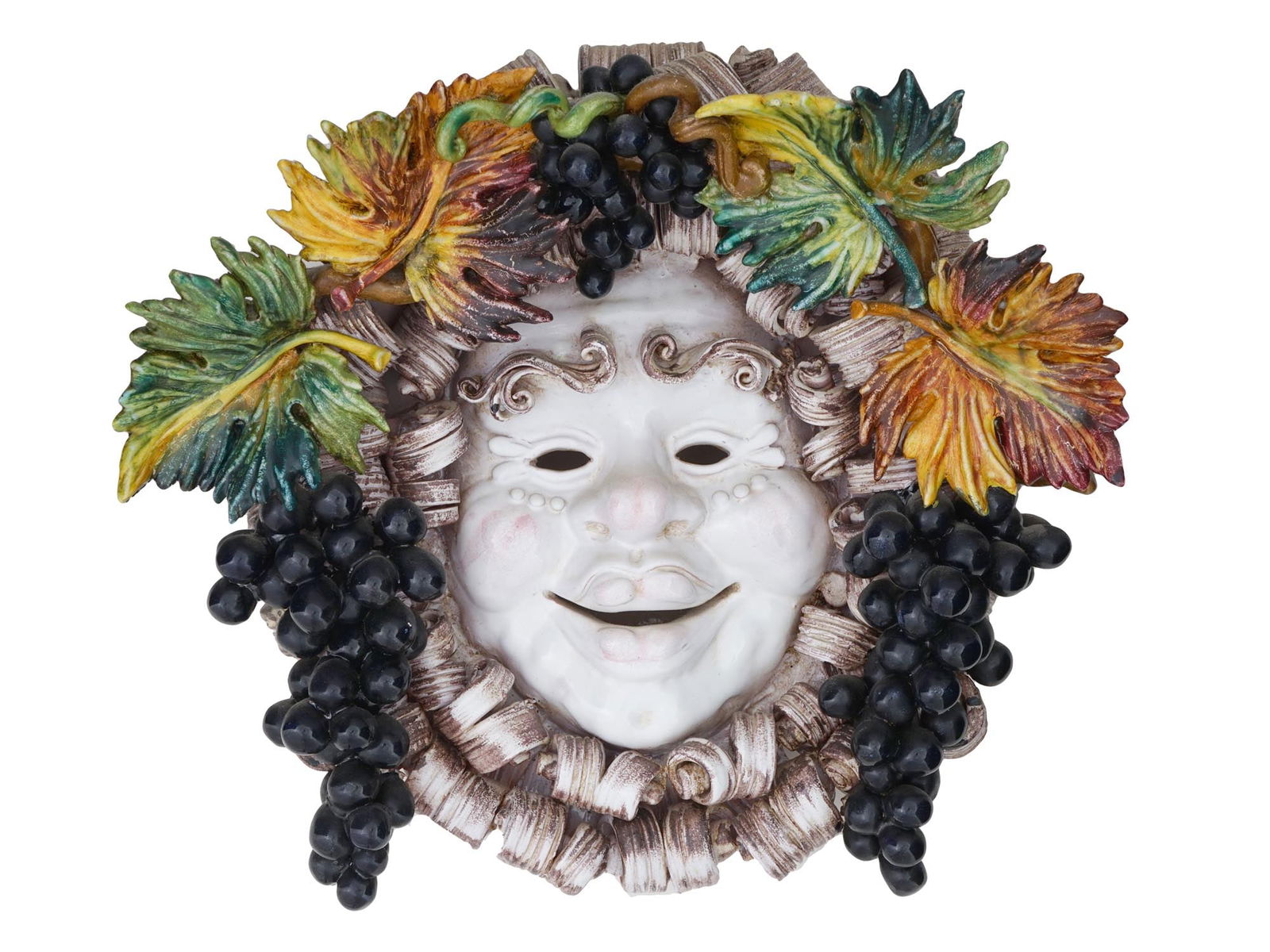 ITALIAN MAJOLICA BACCHUS MASK EARTHENWARE WALL PLAQUE: A vintage Italian Majolica glazed earthenware mask wall plaque. The Bacchus wall hanging mask is formed as a smiling face with a multi coloured crown of fruits, lemons grapes and plumes. Unmarked. Cer