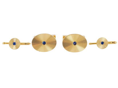 TIFFANY AND CO 14K GOLD SAPPHIRE CUFFLINKS AND STUDS: A vintage 14K yellow gold jewelry set by Tiffany and Co., a pair of bullet-back cufflinks and two shirt studs. Ca. 1940s. Sunburst guilloche disc design with a central round-cut sapphire stone. Each p