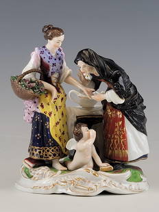 ANTIQUE 19TH C ROYAL VIENNA PORCELAIN GROUP FIGURINE: An antique 19th century Royal Vienna figural group depicting an old palm reader lady beside a maiden holding a basket of flowers by a small tea table bearing a teapot, and a cherub at their feet with