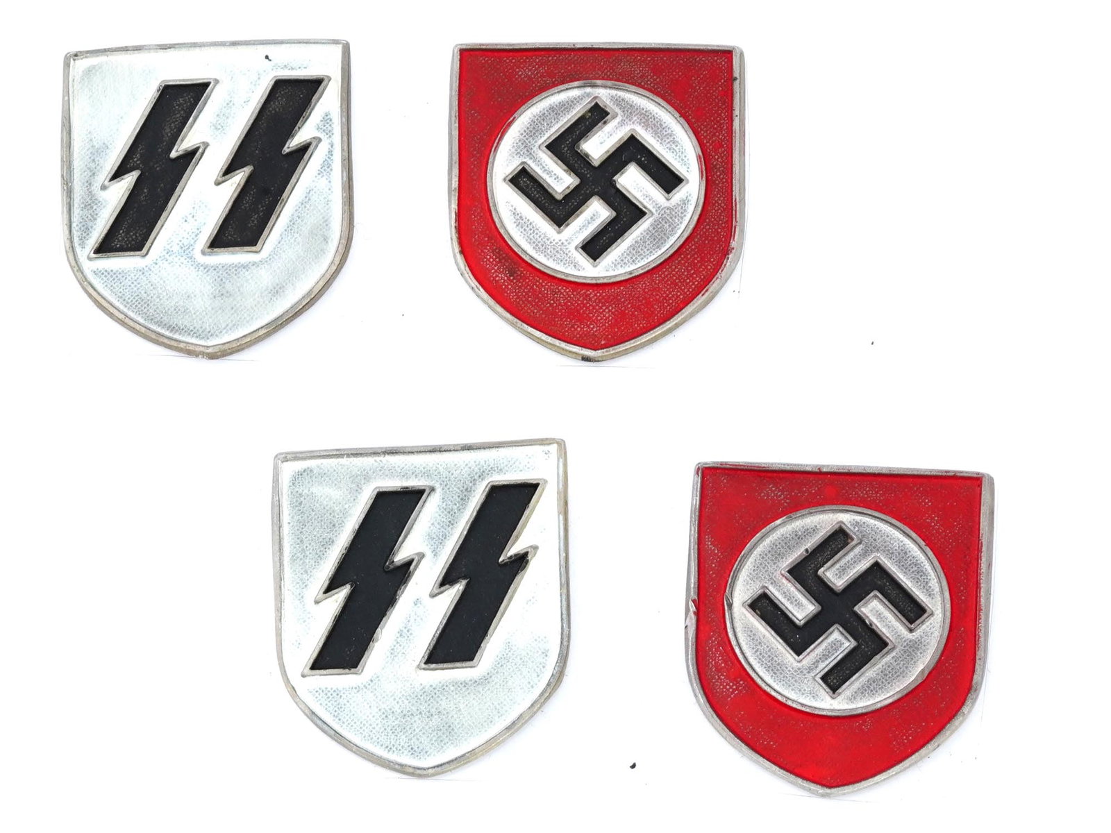 GROUP OF 4 GERMAN WWII SHIELDS FOR SS PITH HELMET: A collection of four WWII Nazi German enamel metal helmet or hat badges. The collection includes a pair of shields for an SS pith helmet, covered with enamel in black and silver shades; and two helmet