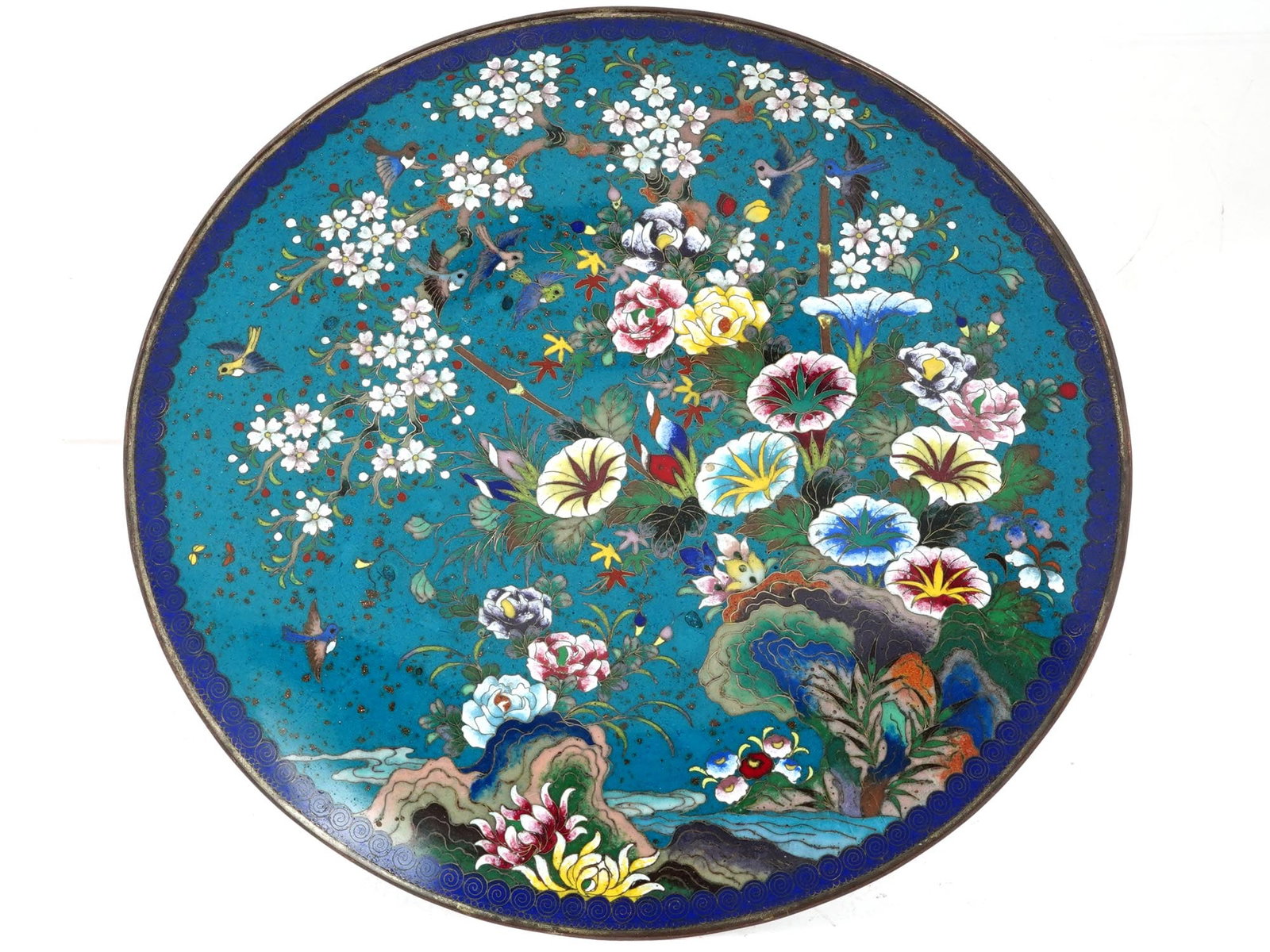 HIGH QUALITY MEIJI JAPANESE CLOISONNE ENAMEL PLATE: A high quality antique Japanese, late Meiji era, enamel plate. The interior of the plate is adorned with a polychrome enamel image of birds flying near a sakura tree with blossoming flowers on a river