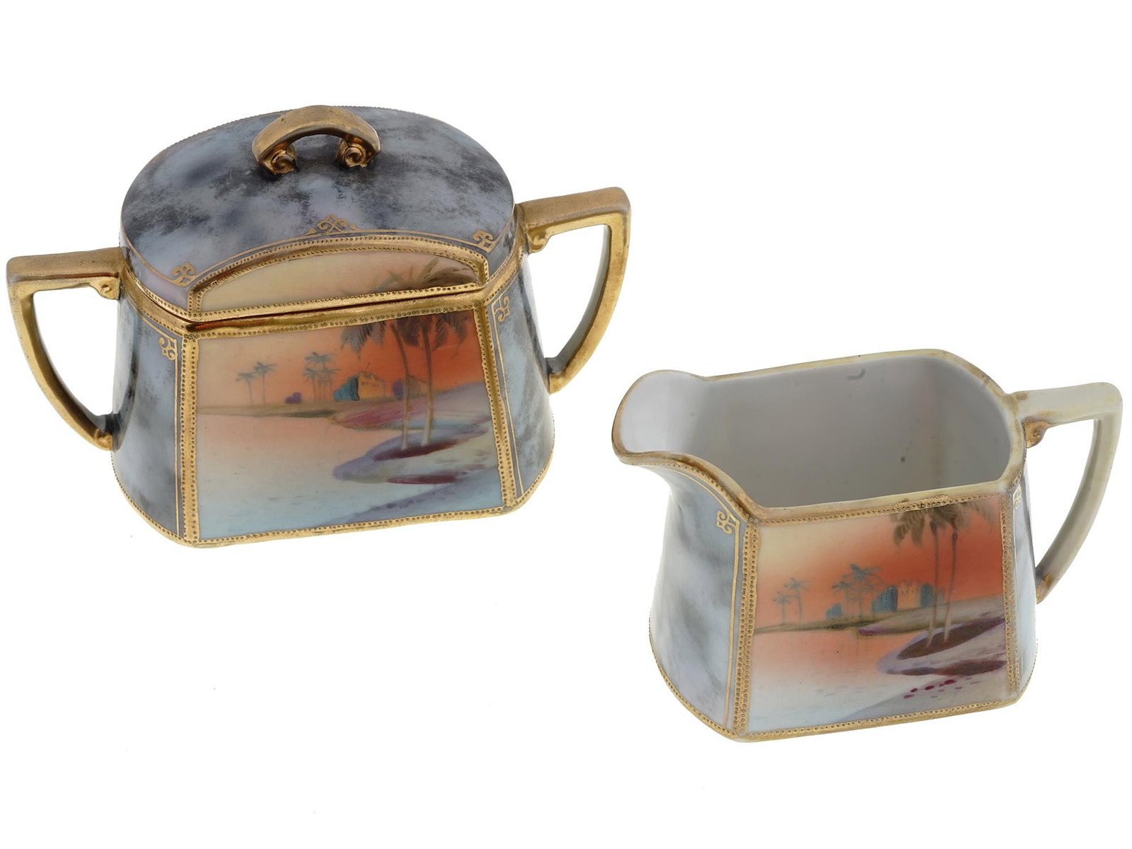 MIDCENT JAPANESE PORCELAIN CREAMER AND SUGAR BOWL: A lot of mid-20th century Postwar Japanese porcelain tableware, a creamer and a lidded sugar bowl. The pieces have a rectangular shape and a matching desert landscape design with gilt rims and handles