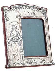 ANTIQUE ART NOUVEAU MANNER ENGLISH SILVER FRAME: An antique Art Nouveau manner English picture or photo frame. The frame is decorated with a relief image of a lady surrounded by flowers in a landscape. Mounted on a wooden base. Marked with Silver li