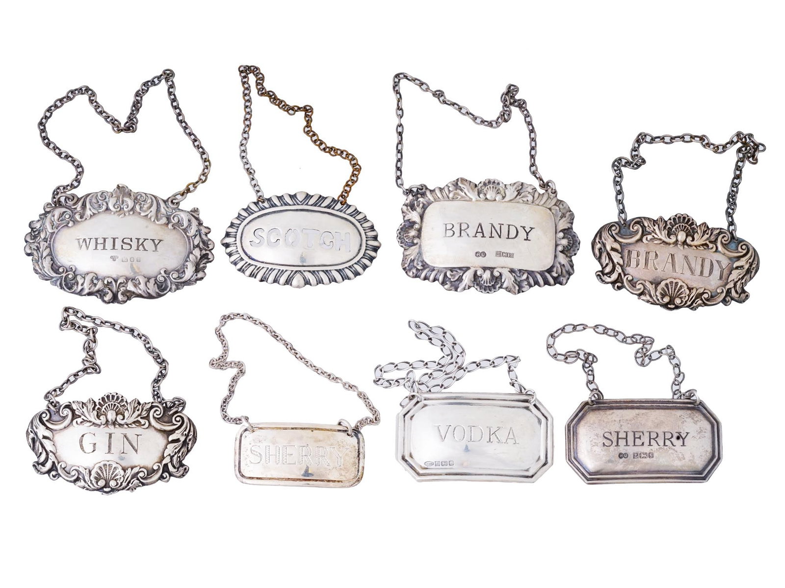 ANTIQUE ENGLISH SILVER LIQUOR TAGS OF VARIOUS DESIGNS: A group of eight antique English silver liquor tags from various manufacturers. Distinguished by their diverse designs, some tags feature delicate floral decorations, showcasing the Victorian eras pen