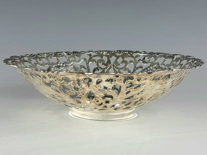 ANTIQUE RETICULATED STERLING SILVER SERVING BOWL: An antique ornate Victorian sterling silver serving bowl or bon bon dish. The bowl is decorated with intricate perforated design, features a repousse floral arrangement at the center, and four vases w