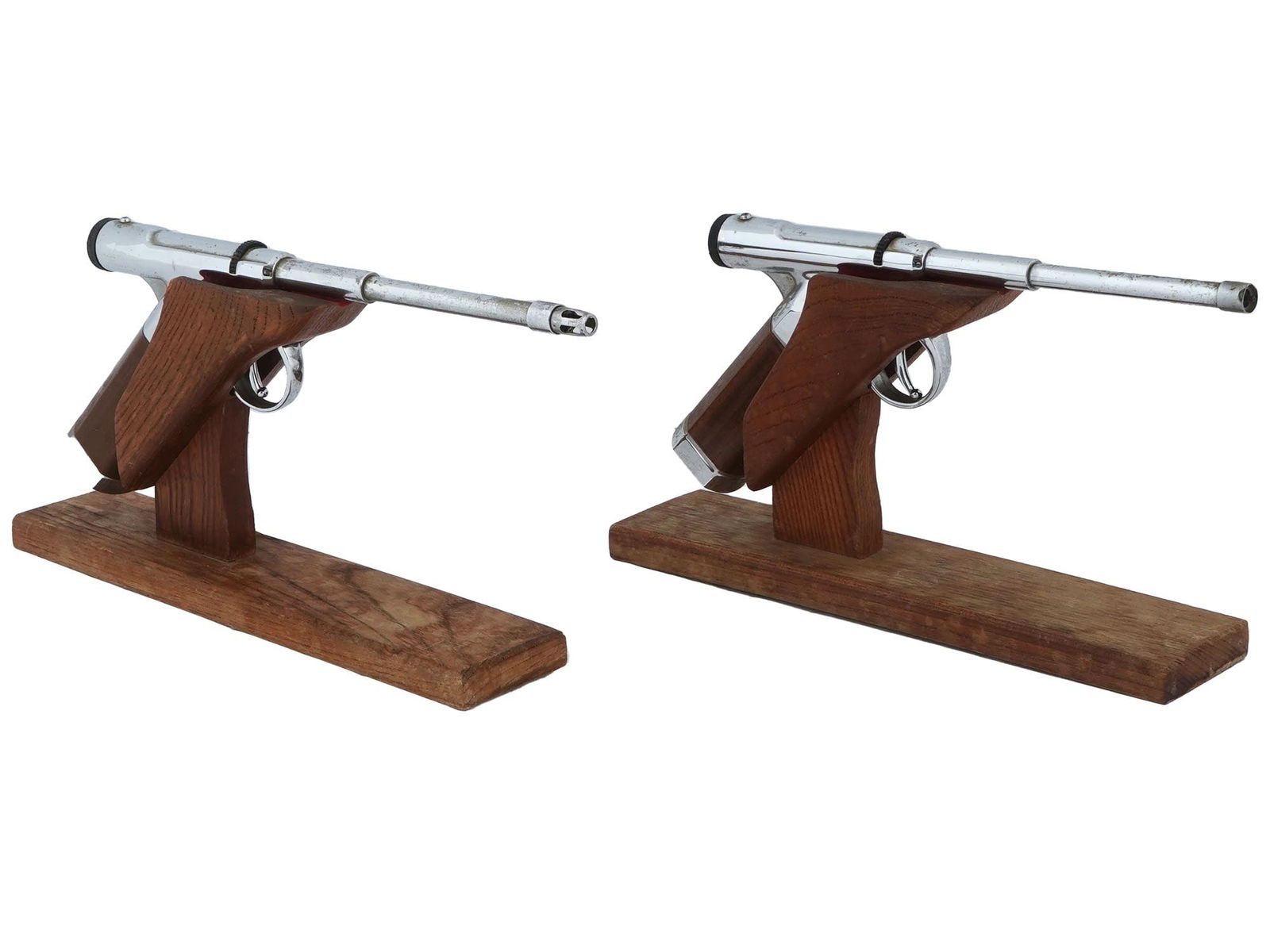 PAIR OF GUN SHAPED TABLE LIGHTERS W WOODEN STANDS: A pair of vintage gun shaped table lighters with wooden stands. Silver toned lighters with wooden handles. Resembles the shape of the American Eagle 9mm Luger made by Stoeger. Lights up when the gun t