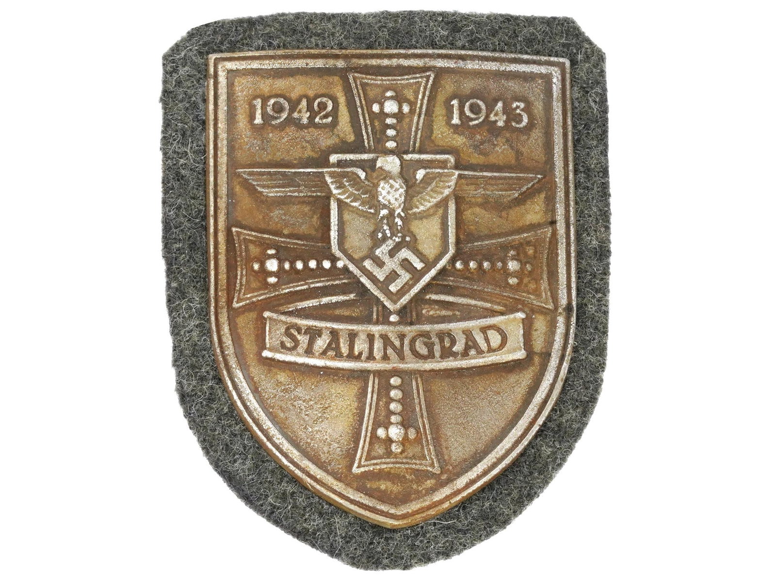 WWII NAZI GERMAN MILITARY AWARD STALINGRAD SHIELD: A WWII German military decoration, the Stalingrad Shield. The zinc shield-shaped badge features an eagle with with swastika, a cross, and an inscription 1942 1943 Stalingrad. The Battle of Stalingrad 