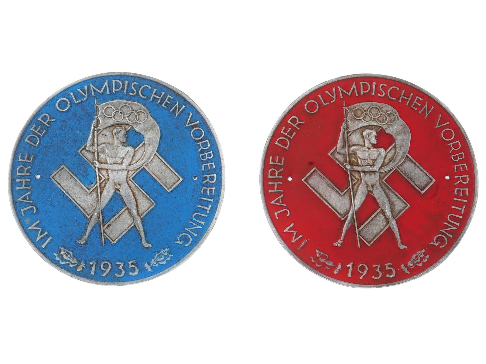 SET OF 2 GERMAN BERLIN OLYMPIC GAMES PLAQUES 1935: A set of 2 German Berlin Olympic Games plaques in blue and red, 1935. Both plaques read In The Year Of Olympic Preparation or German: Im Jahre der Olympischen Vorbereitung. The circular plaques depict