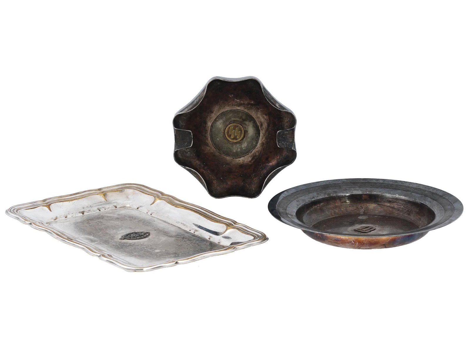 LOT OF THREE GERMAN WWII ITEMS TRAY AND ASHTRAYS: A lot of three German WWII items, the tray and ashtrays. The rectangular tray is in silver tone with raised edges and decoration in the middle. On the reverse side, there is a marking with a Nazi eagl