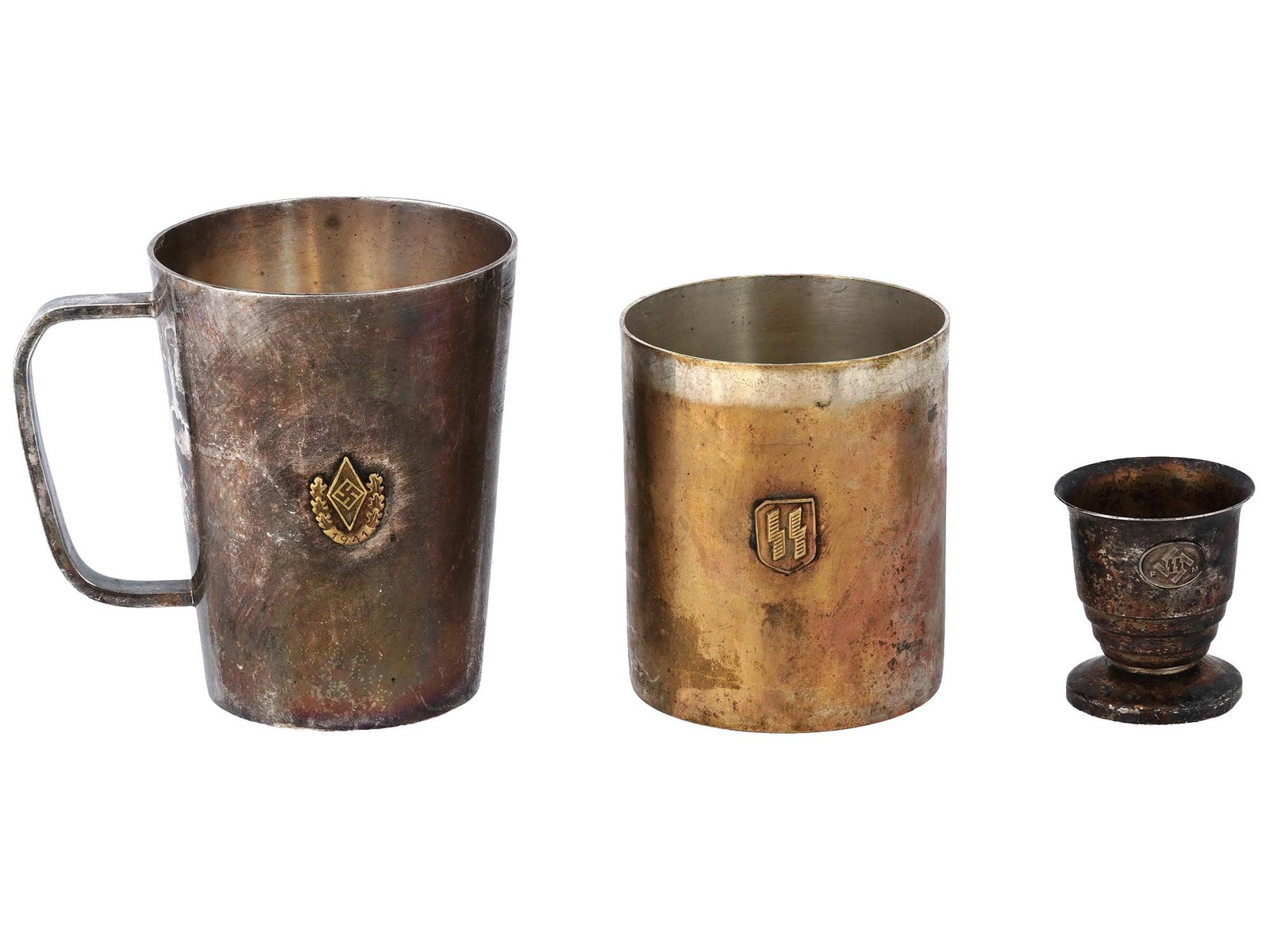 LOT OF THREE GERMAN WWII THIRD REICH METAL CUPS: A lot of three German WWII Third Reich metal cups. The first mug expands at the top, with a handle. In the middle, it is decorated with applied decor of a swastika in a diamond, and below it is a wrea