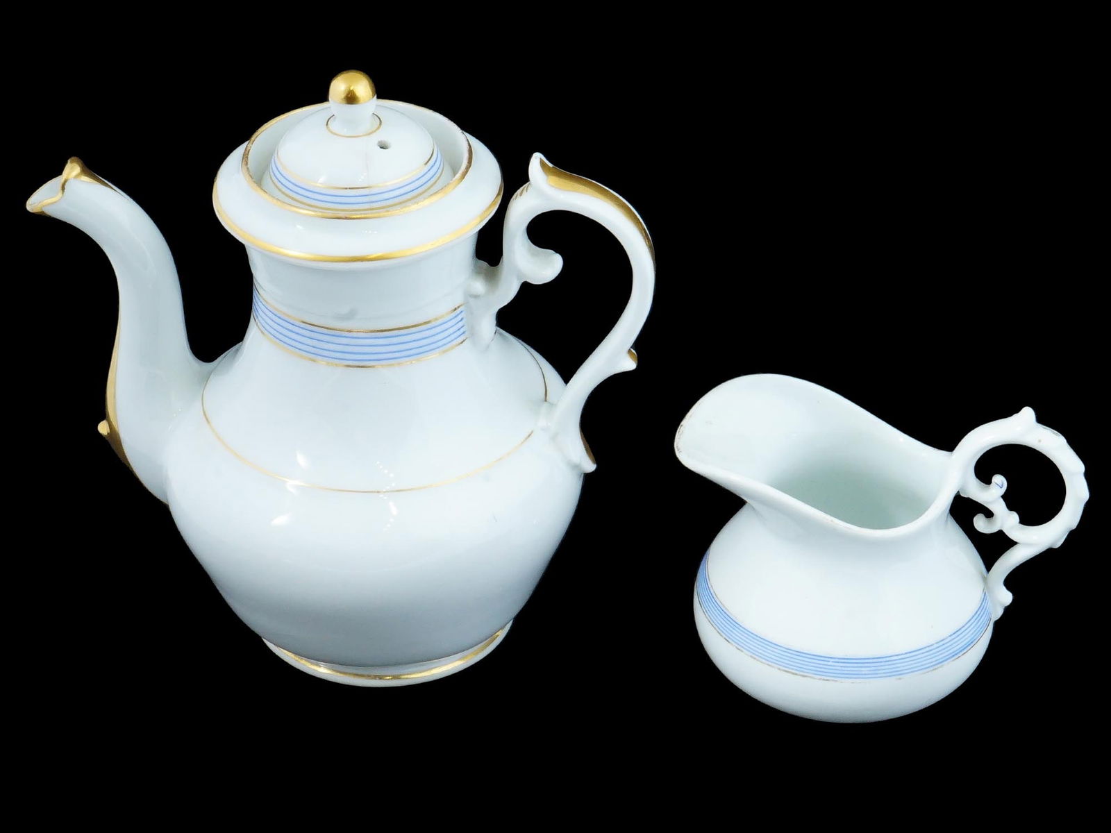ANTIQUE RUSSIAN PORCELAIN TEA SET BY KORNILOV BROS: A matching pair of antique Russian porcelain tea serveware manufactured by Kornilov Brothers. White teapot and creamer with figurative handles. Gilt accents on the handles, spouts and rims. Blue bands