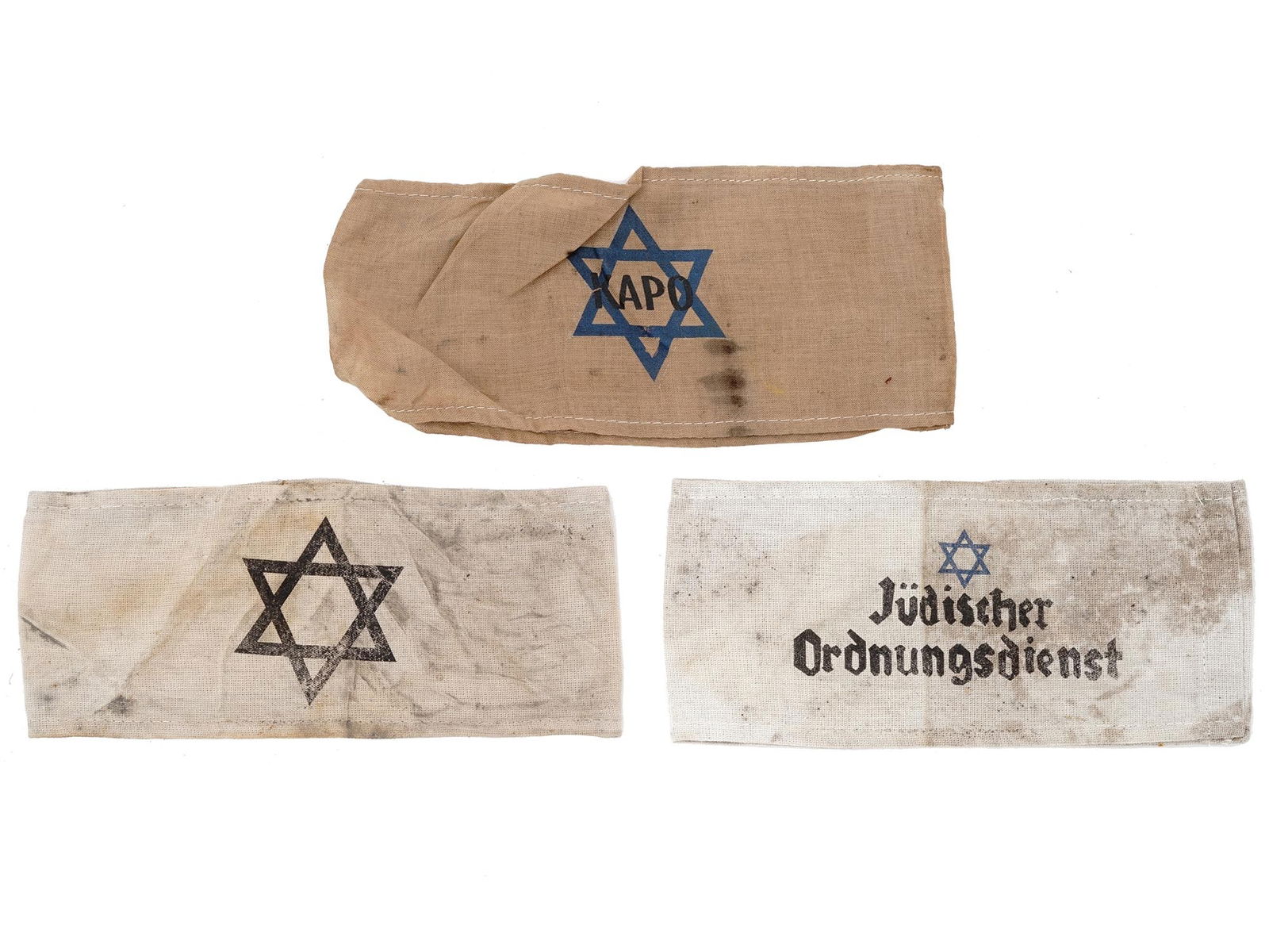 WWII HOLOCAUST CONCENTRATION CAMP ARMBANDS 3 PCS: Three WWII Jewish concentration camp fabric armbands. The first features a Magen David. The second has a Magen David with the inscription Kapo. The third has a Magen David with the inscription Judisch