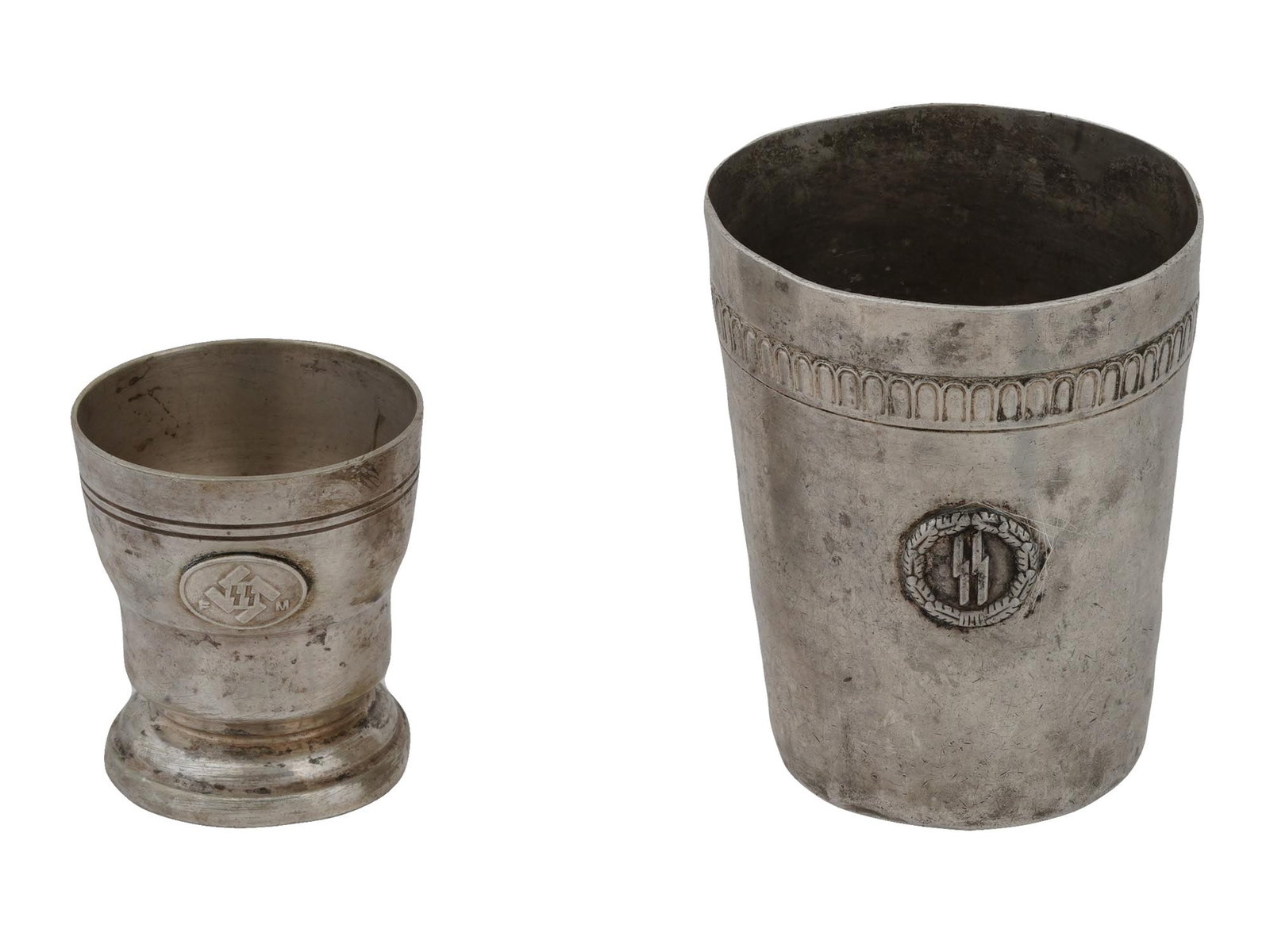 TWO WWII NAZI GERMAN ERA WAFFEN SS CUPS BY WISKEMANN: A lot of two Nazi German Third Reich era beaker cups, probably silver plated. The larger cup is decorated with a carved rim and an applied SS runes in an oak wreath, marked on the bottom: B. Wiskemann
