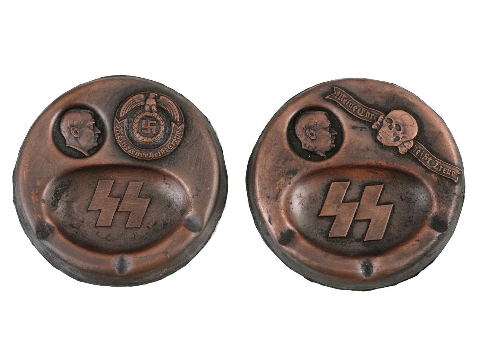WWII NAZI GERMAN THIRD REICH ERA MODEL ASH TRAYS: A pair of WWII Nazi German Third Reich model Waffen SS ashtrays. The ashtrays feature relief designs of a profile portrait of Hitler, a Totenkopf skull with the motto, a Nazi eagle clutching a swastik