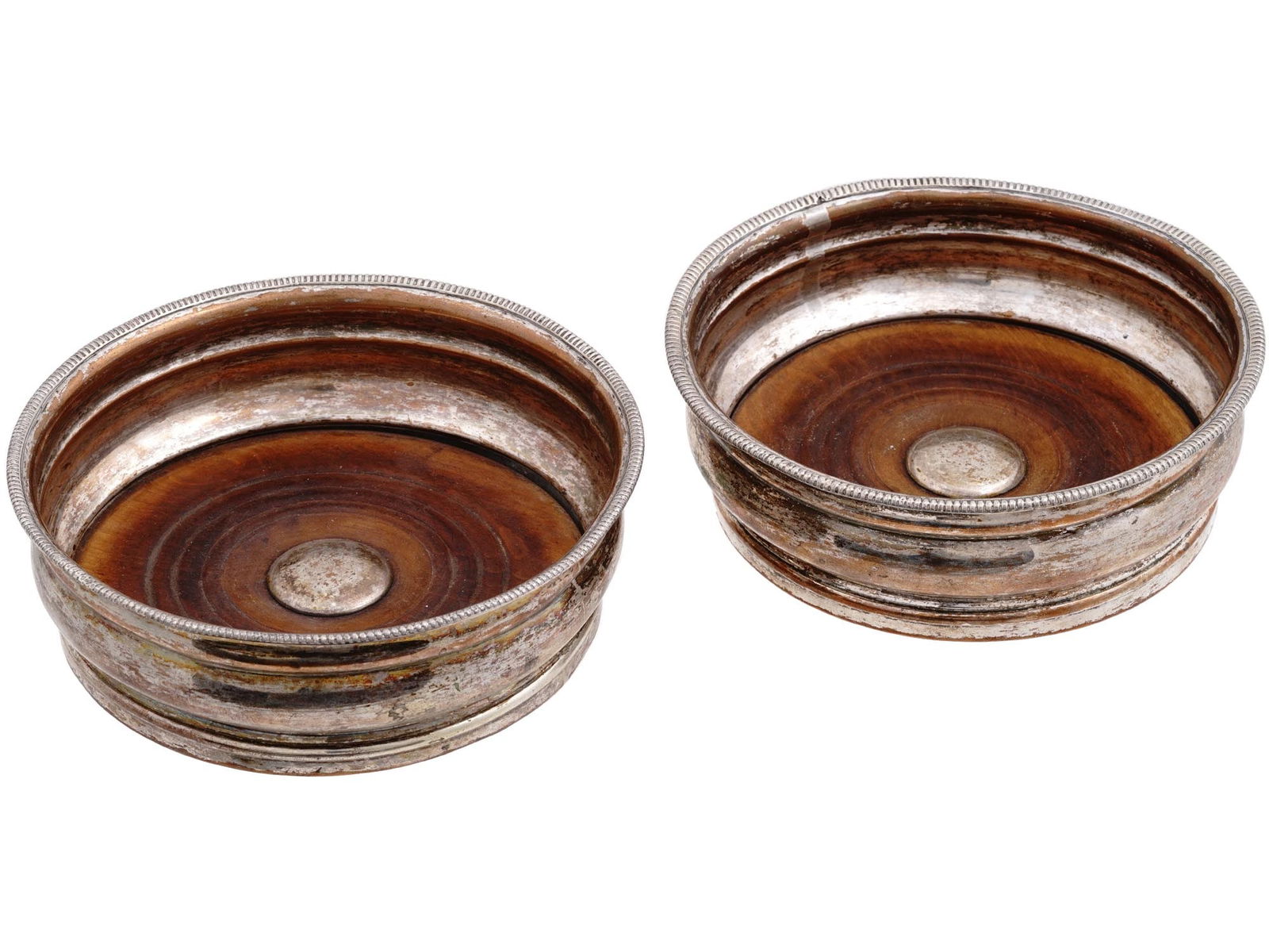 EARLY 20TH CENTURY SILVER PLATED BOTTLE COASTERS: A pair of antique early 20th-century silver-plated bottle coasters. Wooden bases, barrel-shaped sides with ornamented rims. Bottle stands or wine coasters are used as a decorative housing a decanter.