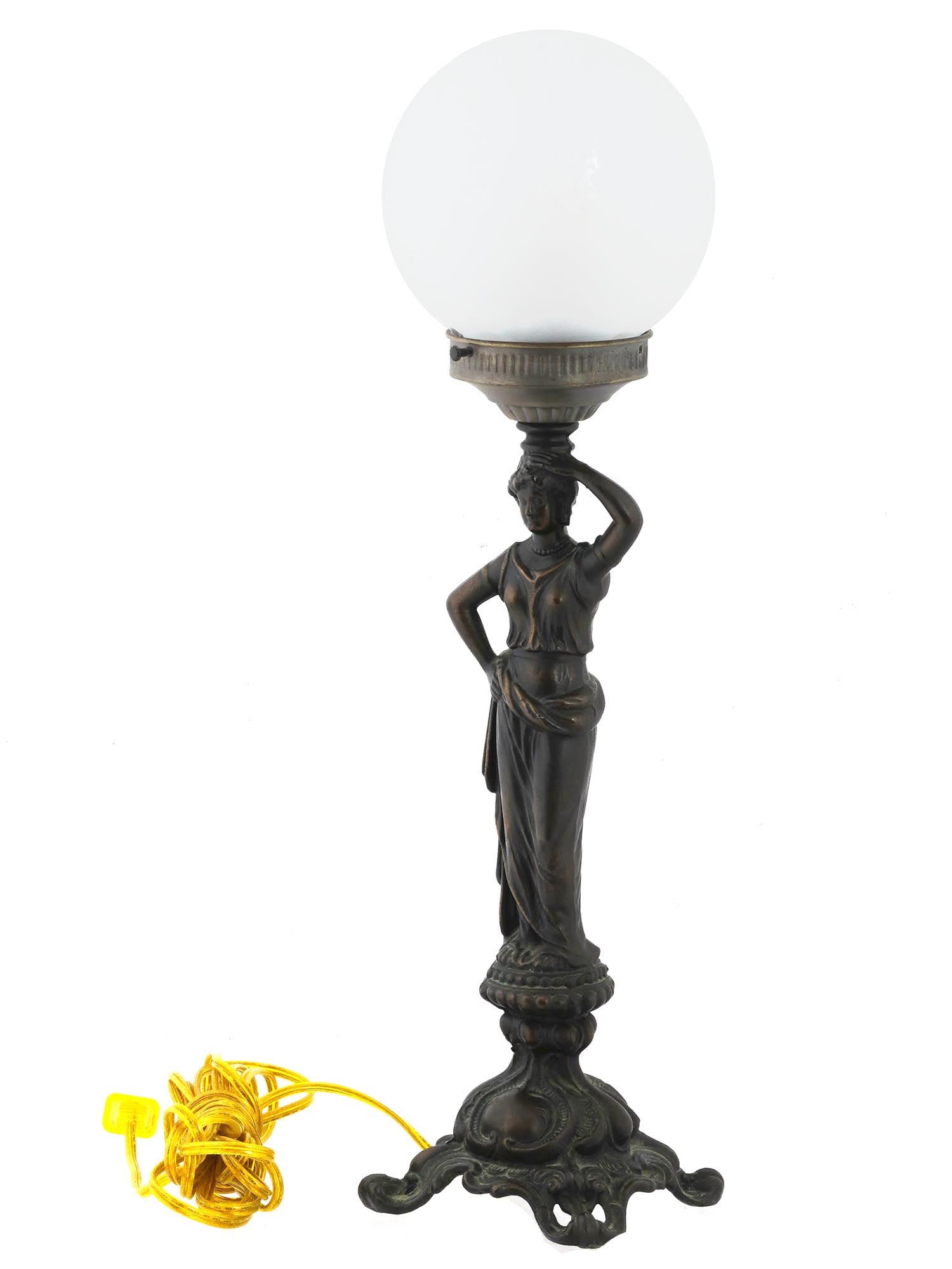 VINTAGE METAL DESK LAMP IN SHAPE OF GREEK NYMPH: A vintage metal desk lamp in the shape of a Greek nymph with a ball shaped lamp shade over her head. The girl is dressed in light long clothes, holds one hand at her side, and raises the other above h