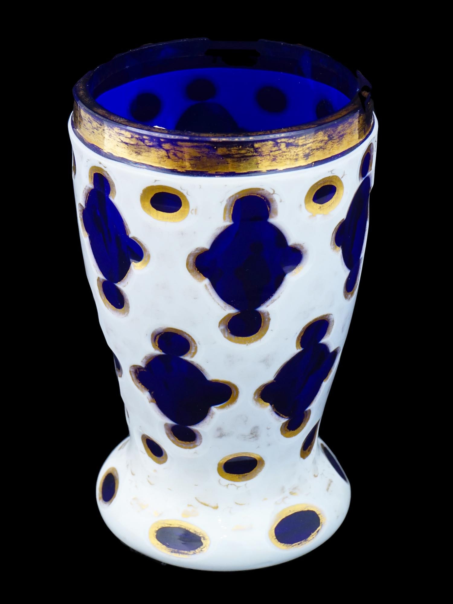 ANTIQUE BOHEMIAN BIEDERMEIER CUT BLUE GLASS BEAKER: An antique Biedermeier blue glass beaker, characterized by a widened rim, narrowed middle, and round base. The beaker is cut and overlaid with opal glass, featuring transparent recesses for creating g