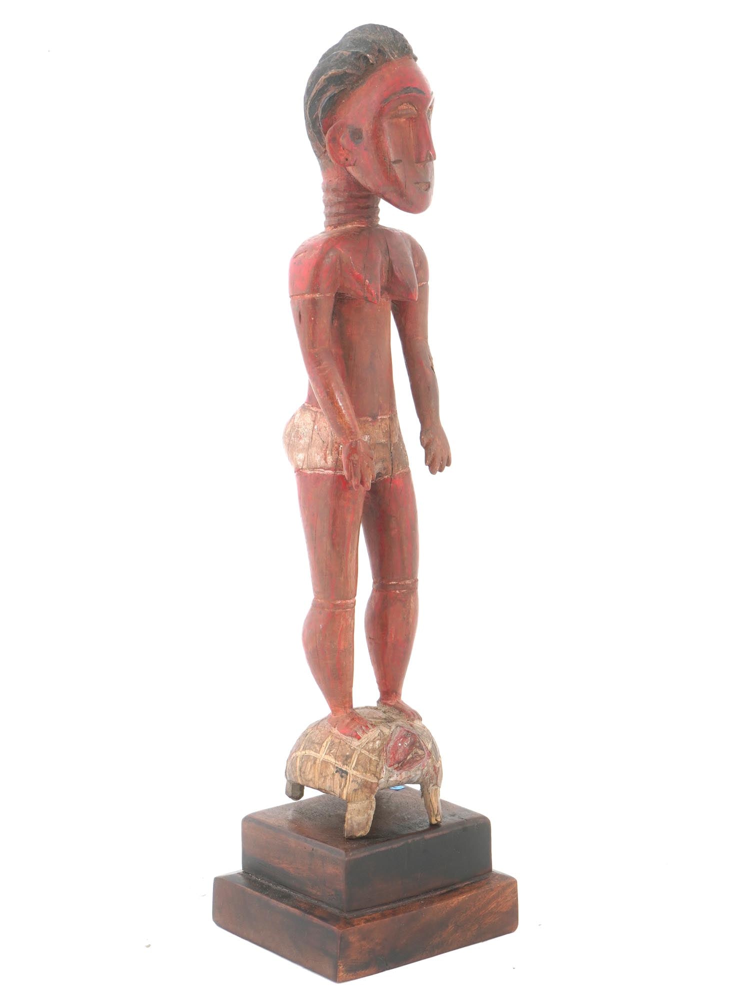 WEST AFRICAN BAULE CARVED RED WOOD FEMALE FIGURINE: A West African figurine from the Baule or Baolet people. The figurine is modeled in the form of an anthropomorphic female figure with classic Baule features.standing on a turtle. The figurine is cover