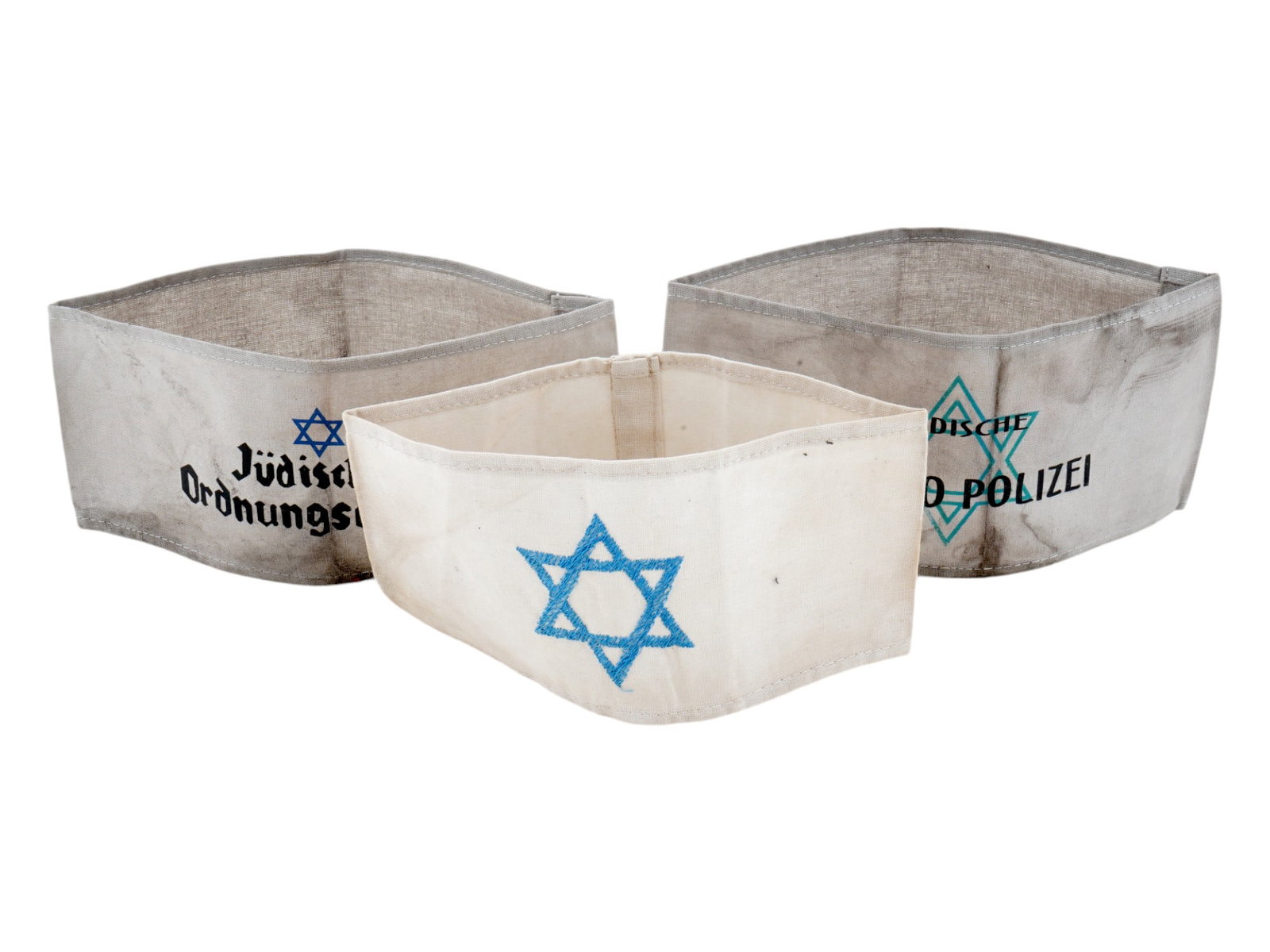 WWII MODEL HOLOCAUST CONCENTRATION CAMP ARMBANDS: A lot of three World War II type Jewish concentration camp fabric armbands. The first has a hand-emboridered Magen David. The second has a Magen David with inscription Judische Ghetto Polizei, Jewish 