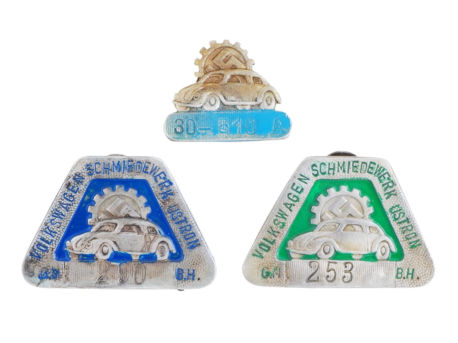GERMAN WWII TYPE THIRD REICH VOLKSWAGEN FACTORY BADGES: A group of three WWII type Nazi German Third Reich Volkswagen factory employee shields. Two badges are covered with enamel in green or blue shades, featuring an image of a car with a swastika insignia
