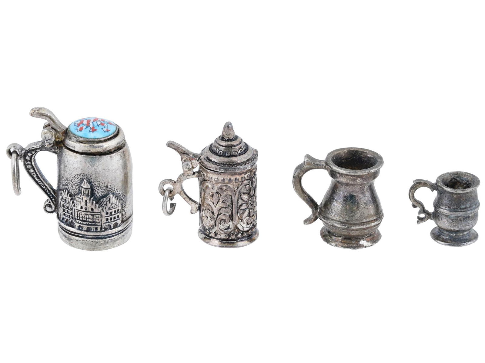 MINIATURE VTG MID CENTURY GERMAN SILVER TANKARDS: A lot of four German miniature silver tankards, each intricately designed with unique details. The first tankard, labeled Frankfurt, features an eagle relief emblem on the front, relief houses on the