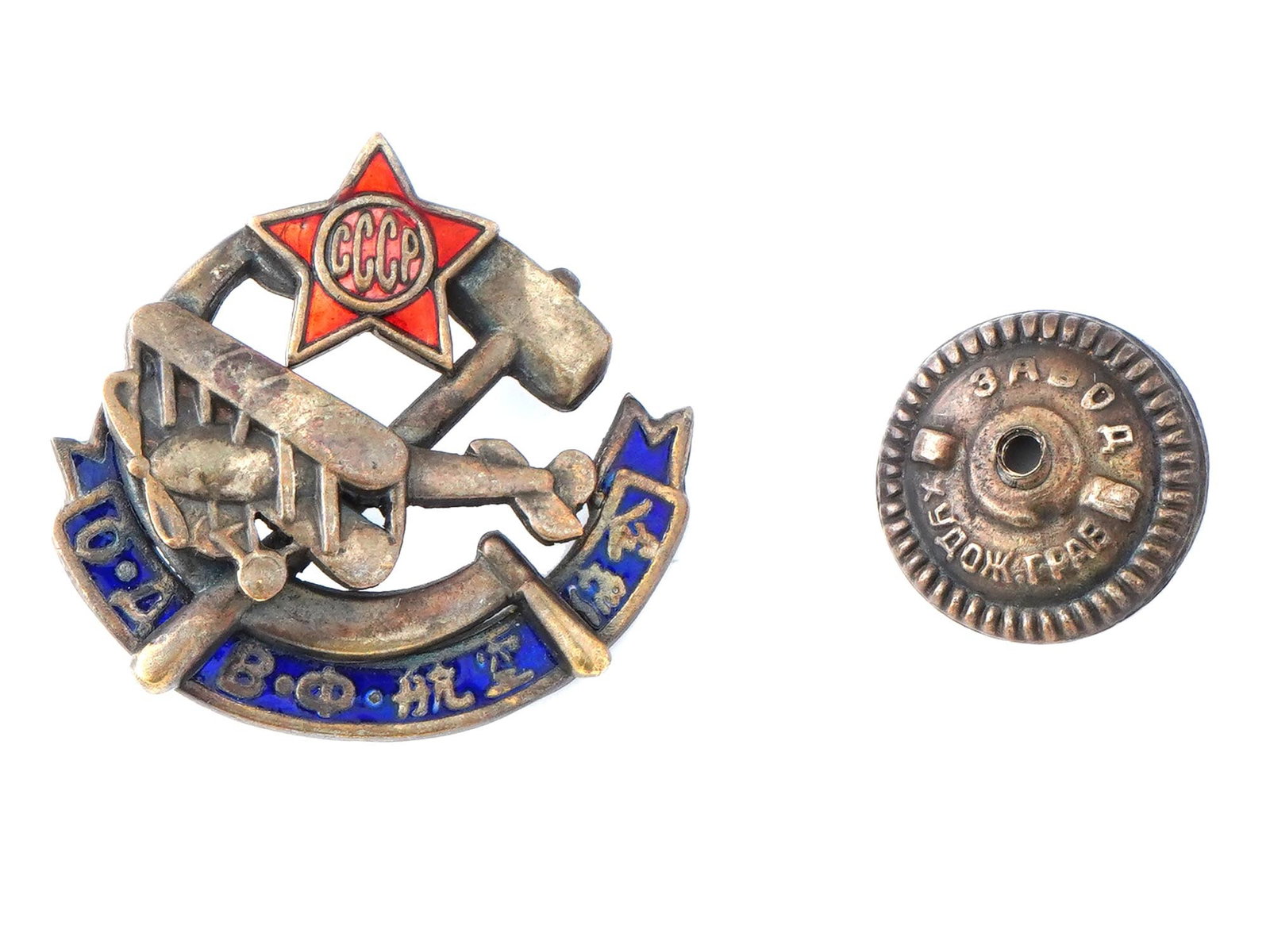 RUSSIAN SOVIET SOCIETY OF FRIENDS OF AIR FLEET BADGE: A Russian Soviet military badge of the Society of Friends of the Air Fleet, crafted from enameled bronze. The badge is modeled as an airplane on a hammer and sickle, with a red star bearing the inscri