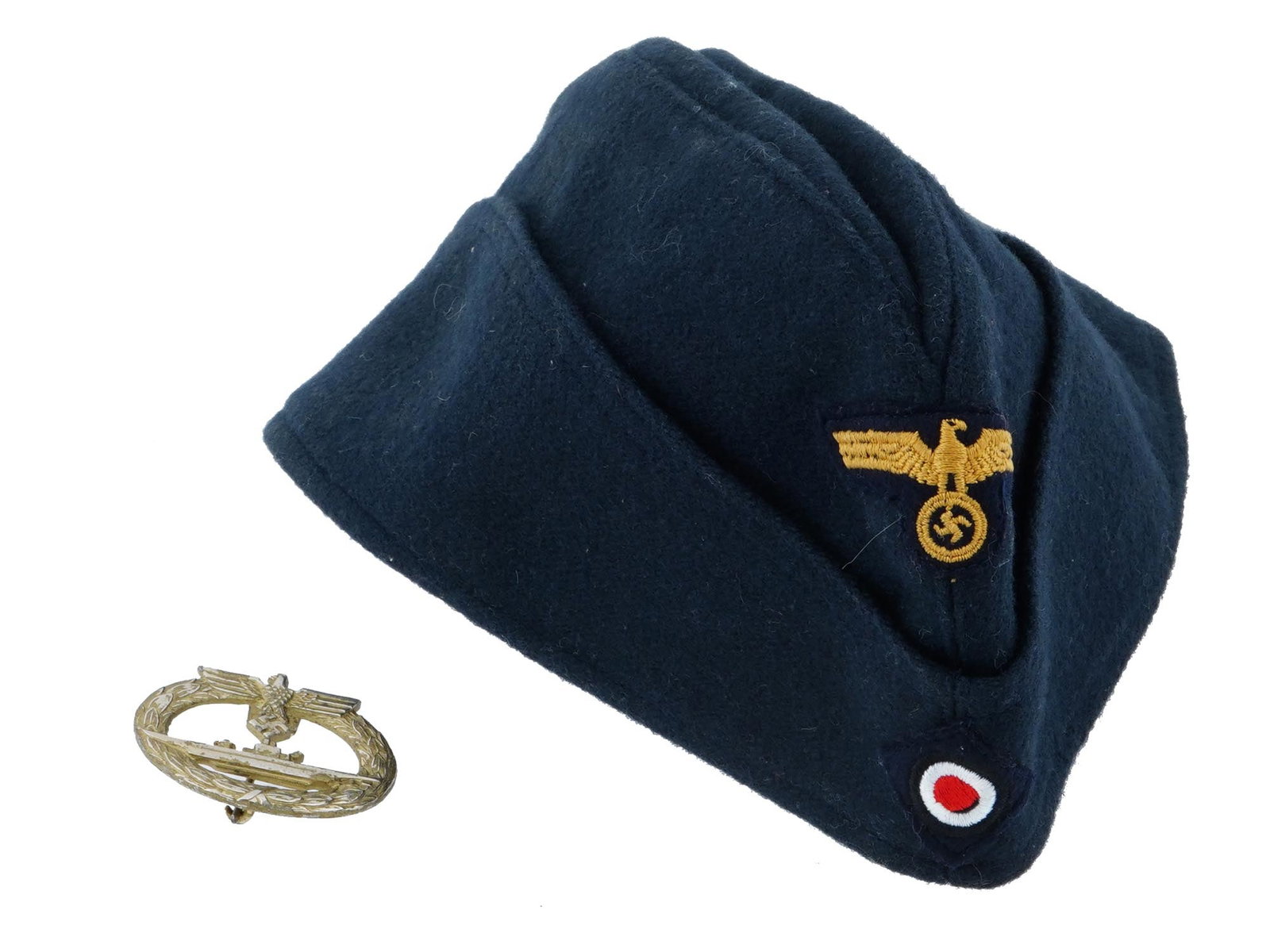 WWII GERMAN KRIEGSMARINE OFFICERS SIDE CAP W BADGE: A WWII Nazi German Kriegsmarine officers side cap. The exterior of this cap is constructed of a fine wool fabric, in a typical dark blue color. The front of the cap is adorned with a complete set of i