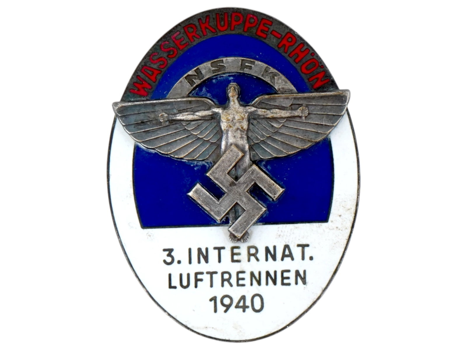 GERMAN WWII NSFK 3RD INTERNATIONAL AIR RACE BADGE: A WWII Nazi German Third Reich era 1940 NSFK Luftrennen Third International Air Race badge. The badge is covered with enamel in blue, white and red shades. The item is adorned with an image of a man w