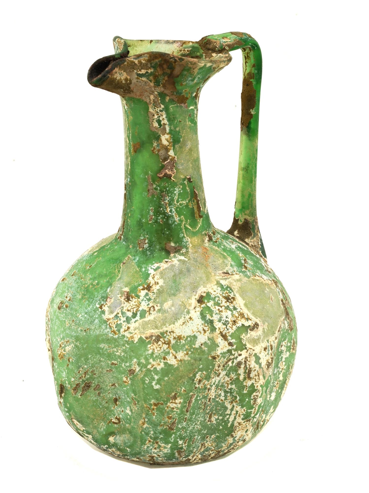 ANCIENT ROMAN GLASS OINOCHOE JUG 100 TO 300AD: An ancient Roman green glass oinochoe jug or pitcher with a ovoid body and curved handle stands on a splayed pedestal foot with tall cylindrical neck and trefoil lip. Circa 100 to 300 AD. This glass e