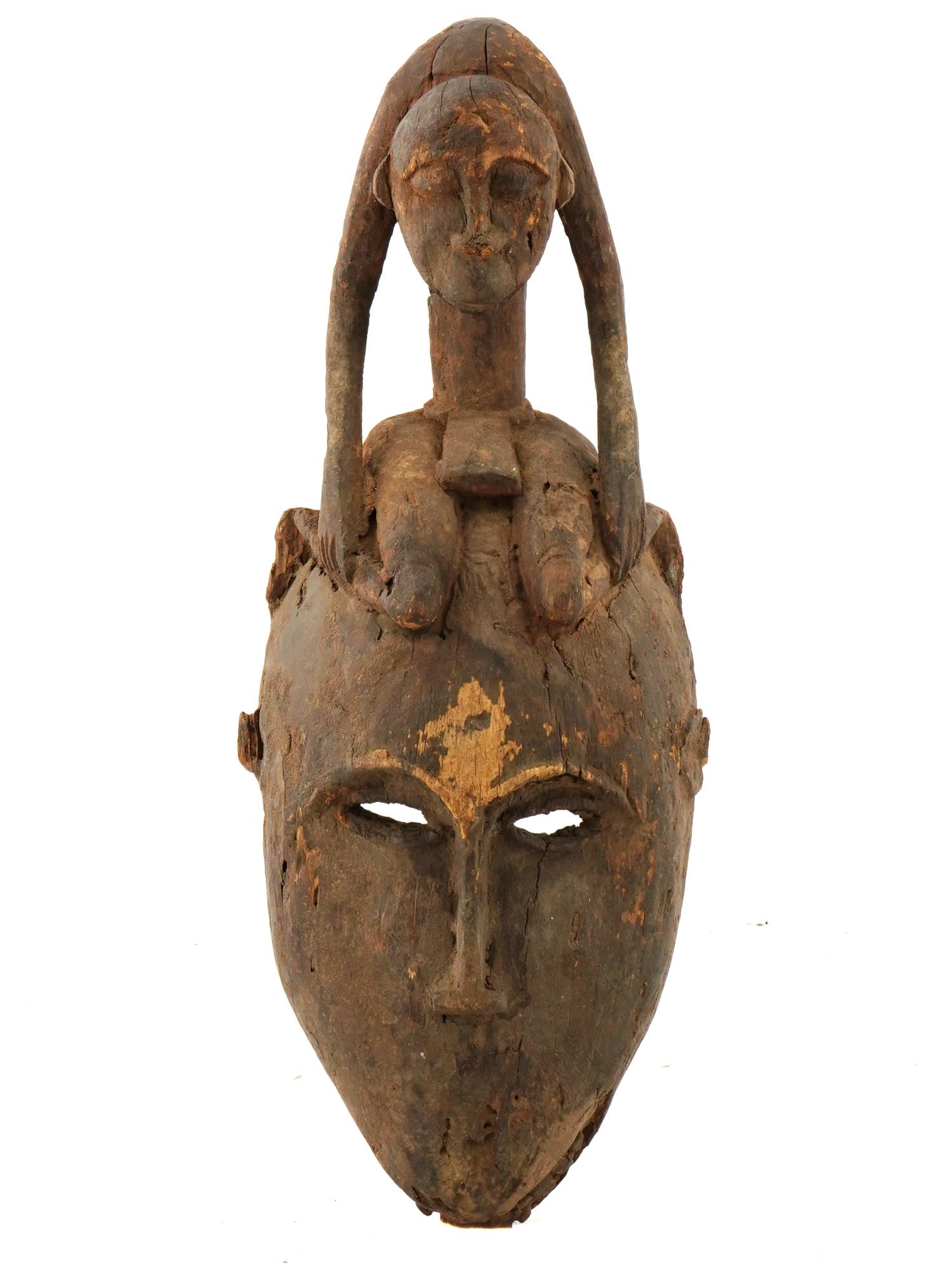 WEST AFRICAN DOGON PEOPLE WOODEN MASK FROM MALI: A West African Dogon wooden mask from Mali. Circa the early 29th century. The mask with narrow eyes and an elongated nose has the seated male figurine on the top of the head. The Dogon people, known f
