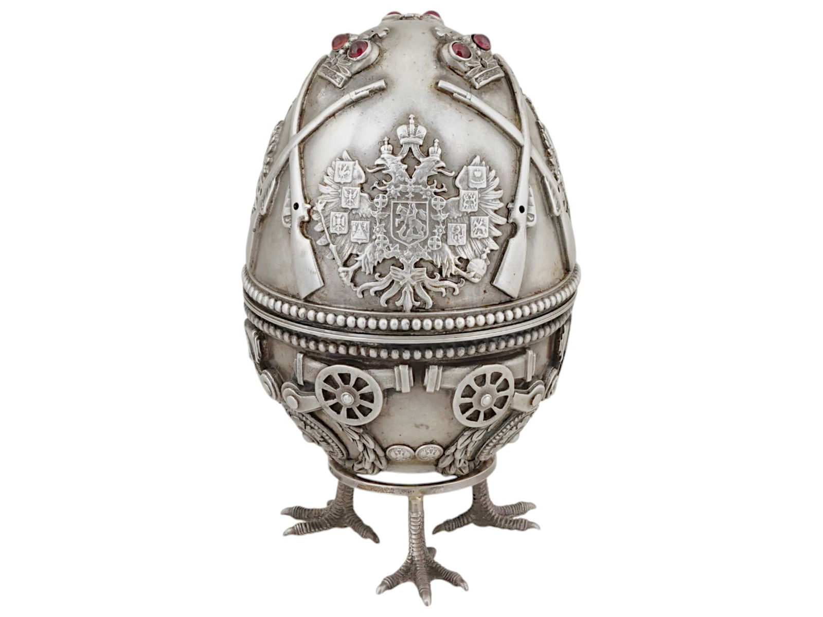 LARGE RUSSIAN SILVER MILITARY EASTER EGG WITH GEMSTONES: A large Russian silver Easter egg consisting of two halves. Richly decorated with relief military symbols such as cannons, guns, coat of arms, and crowns set with gemstones. Hallmarked with the manufa