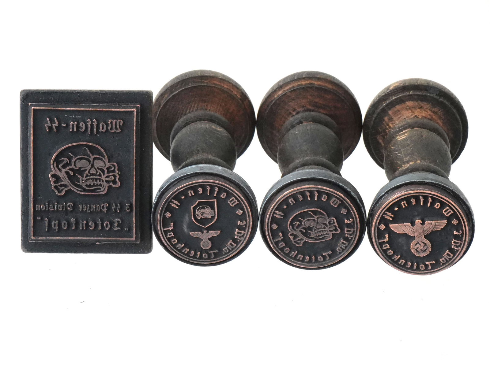 WWII NAZI GERMAN WAFFEN SS TOTENKOPF WOODEN HAND STAMPS: A group of four World War II Nazi German Waffen SS wooden hand stamps, all featuring the insignia of the 3rd Panzer Division Totenkopf. The set includes three round stamps and one rectangular stamp. T